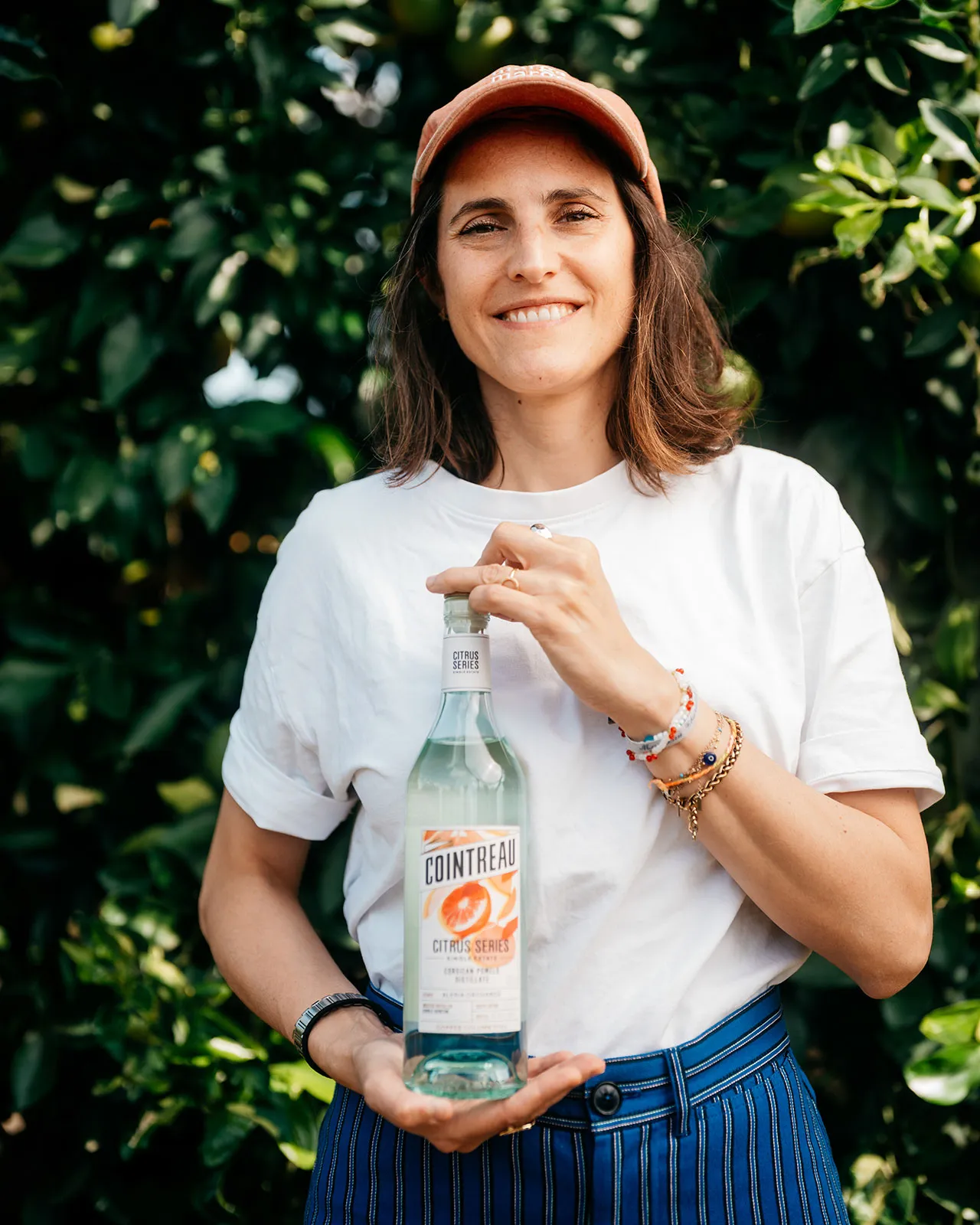 Portrait for Cointreau Cocktail Talks featuring a person holding a bottle of Cointreau Citrus Series in a citrus orchard.