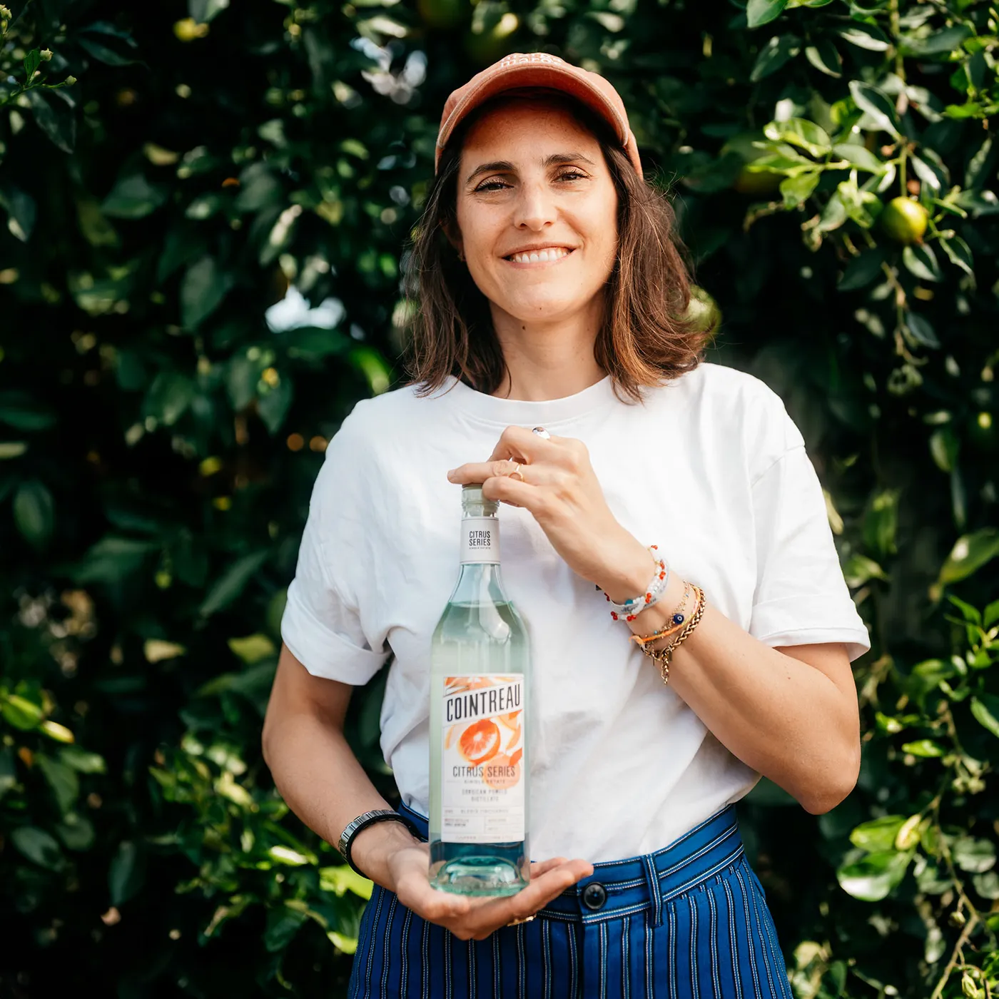 Portrait for Cointreau Cocktail Talks featuring a person holding a bottle of Cointreau Citrus Series in a citrus orchard.