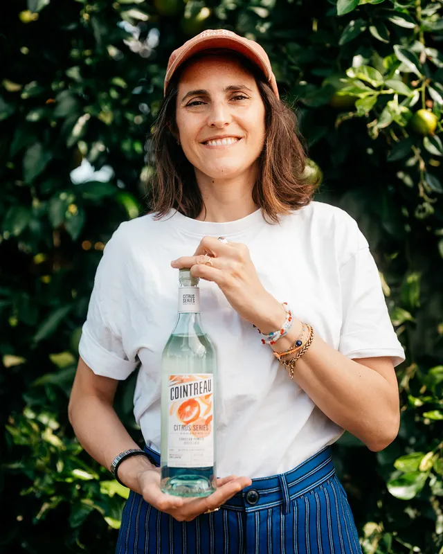 Portrait for Cointreau Cocktail Talks featuring a person holding a bottle of Cointreau Citrus Series in a citrus orchard.