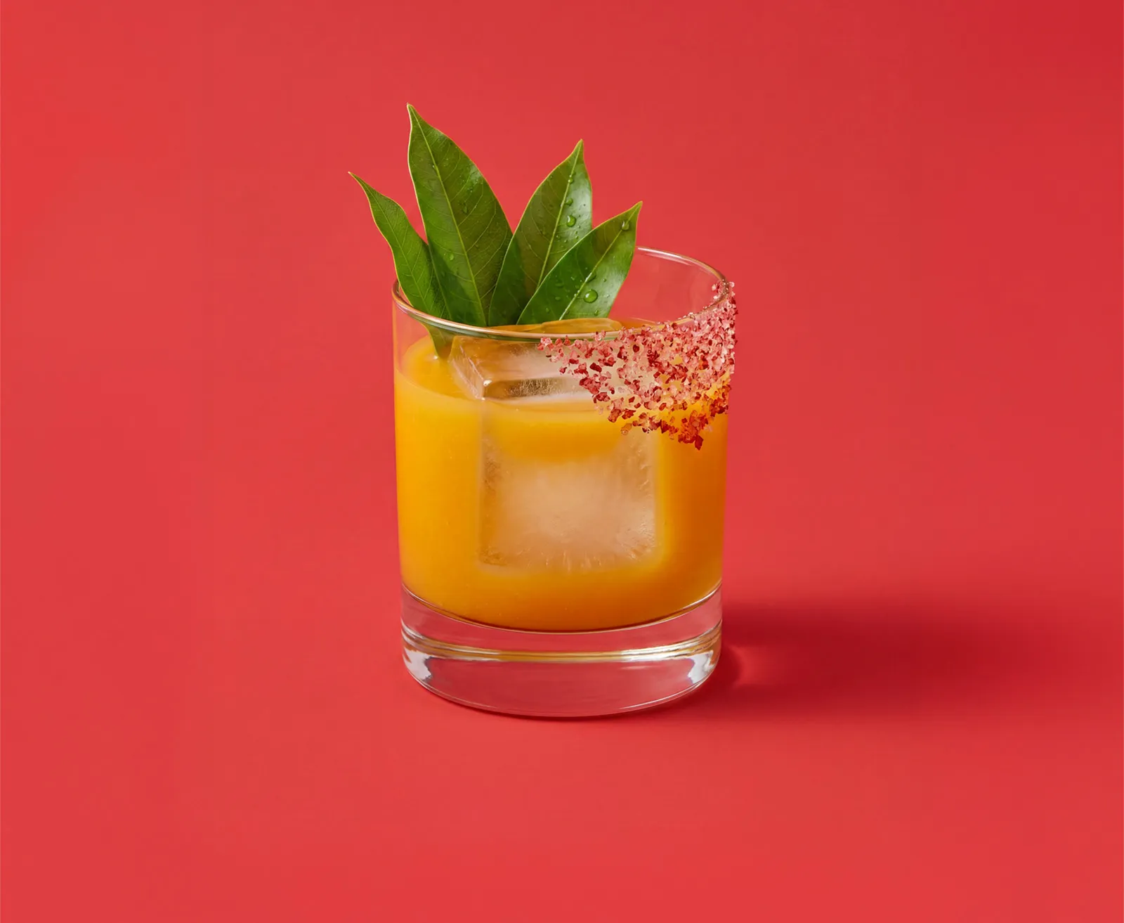 A Spicy Mango cocktail served in a tumbler glass on an hot pink background