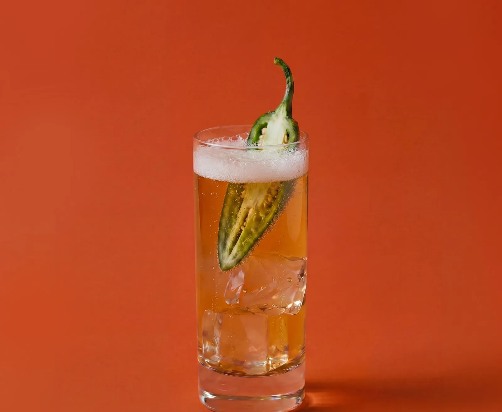 A Spicy Highball cocktail served in a highball glass on an orange background