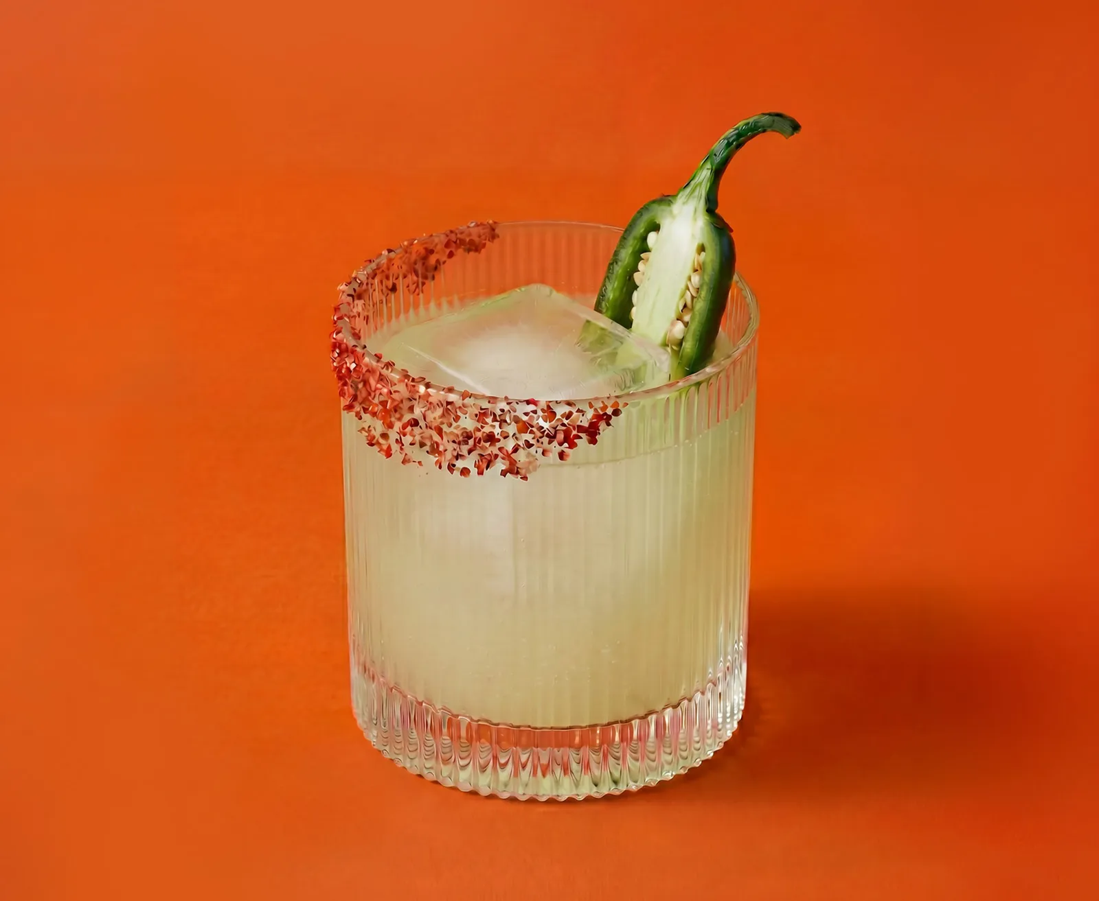 A Spicy Margarita cocktail served in a tumbler glass on an orange background