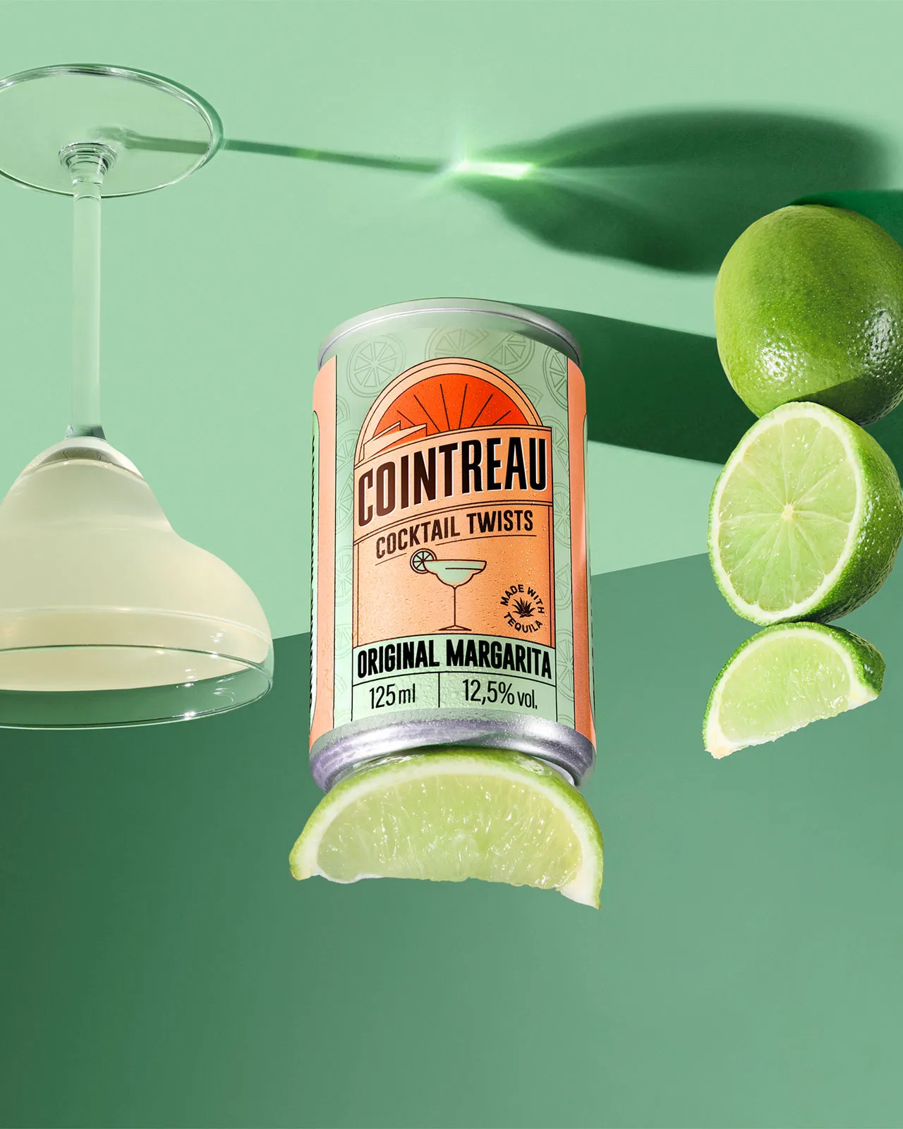 Cointreau Original Margarita can with lime slices and cocktail glass on green background