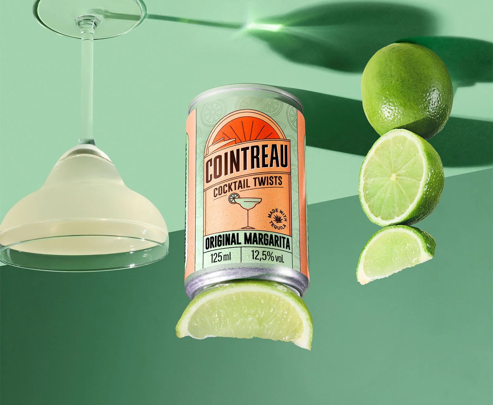 Cointreau Original Margarita can with lime slices and cocktail glass on green background
