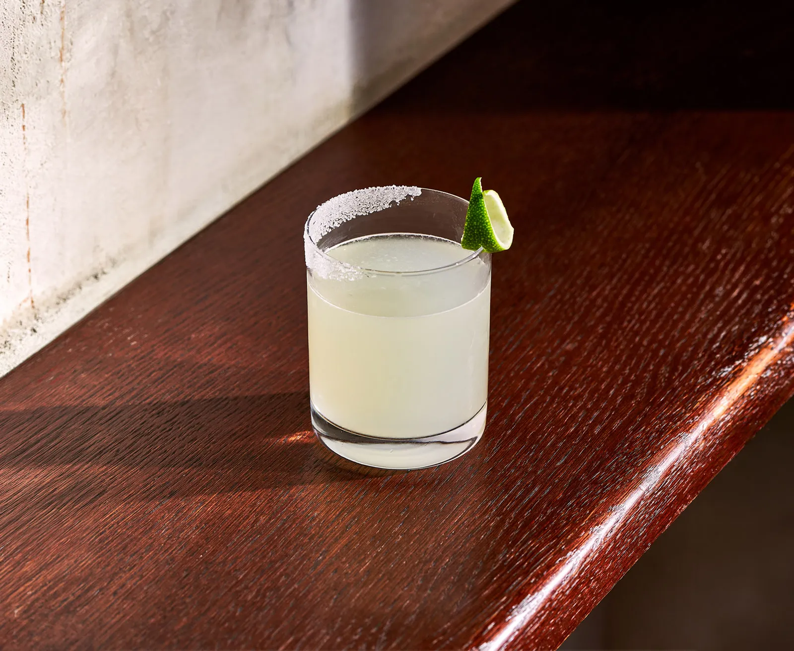 The Original Margarita cocktail with salted rim and lime garnish on wooden bar surface
