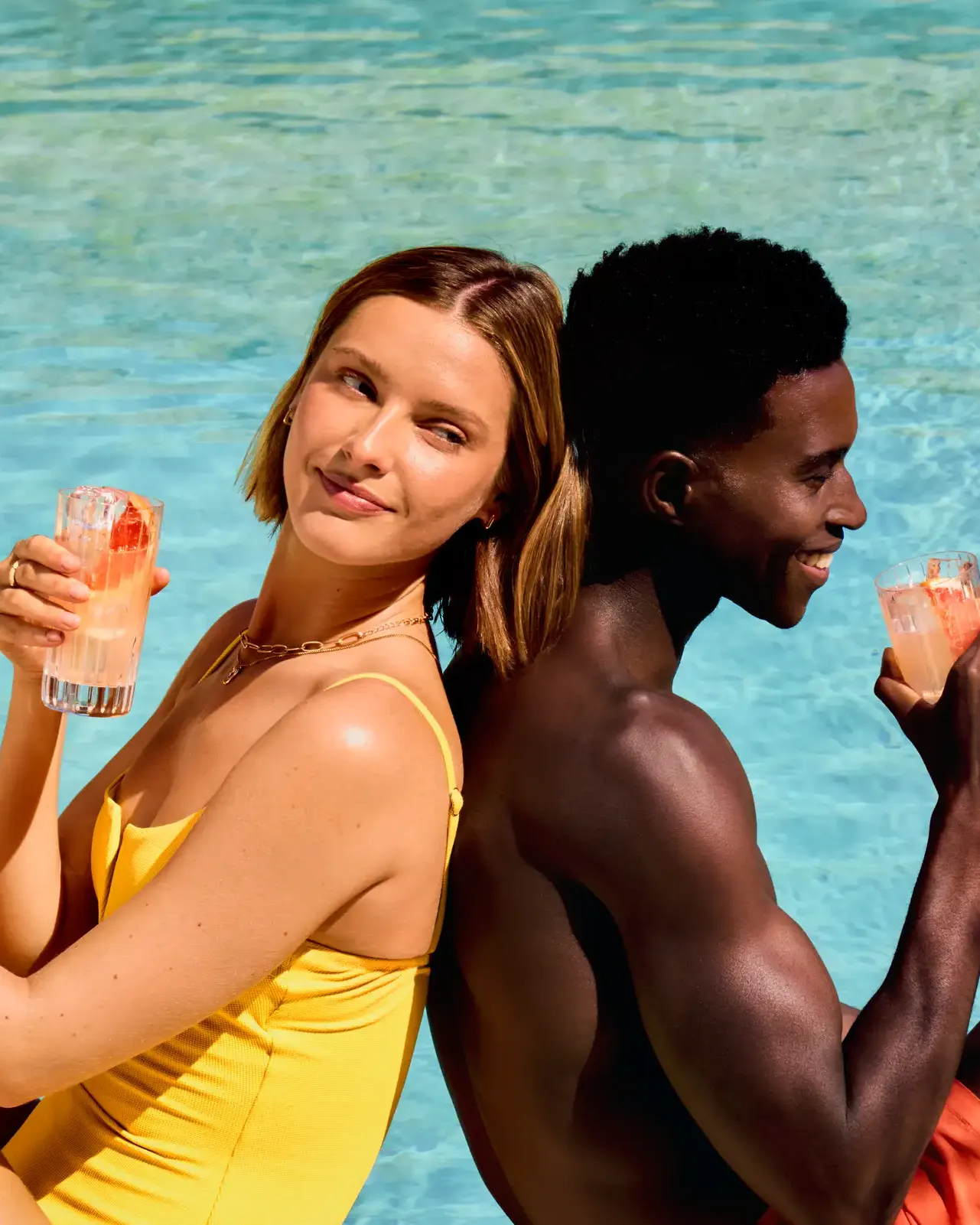 A woman and man relax together by a sparkling pool, enjoying a refreshing cocktail on a sunny day.