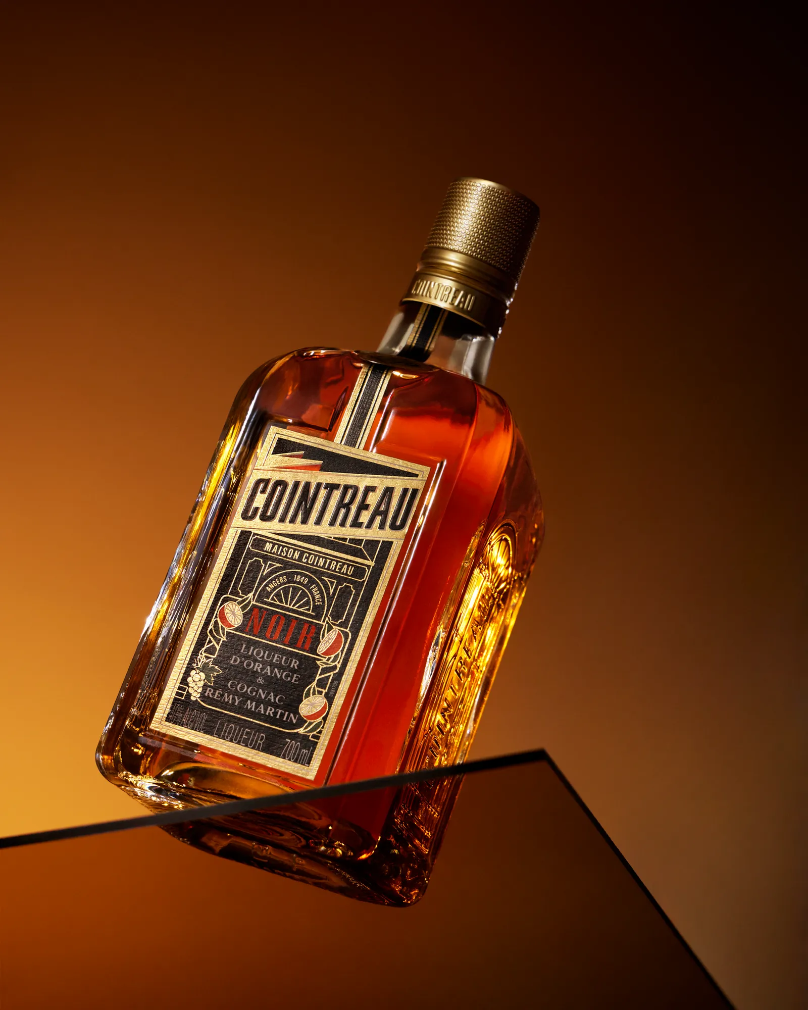 Cointreau Noir bottle angled on glass podium with minimalist orange background and studio lighting
