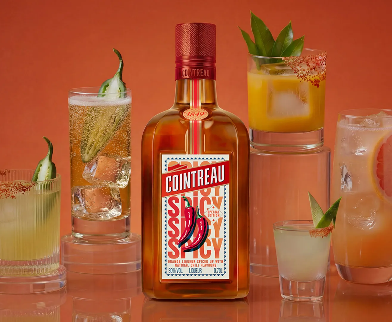 A bottle of Cointreau Spicy with several cocktails on an orange background