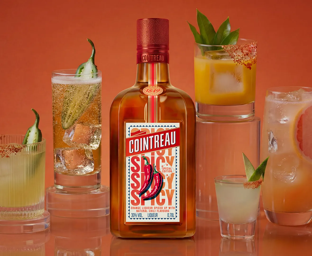 A bottle of Cointreau Spicy with several cocktails on an orange background