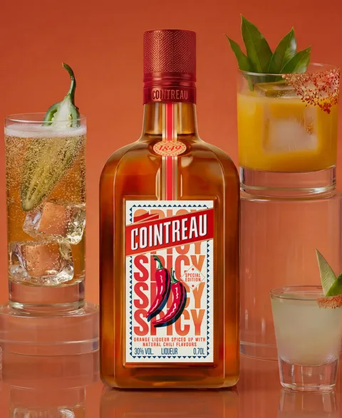 A bottle of Cointreau Spicy with several cocktails on an orange background