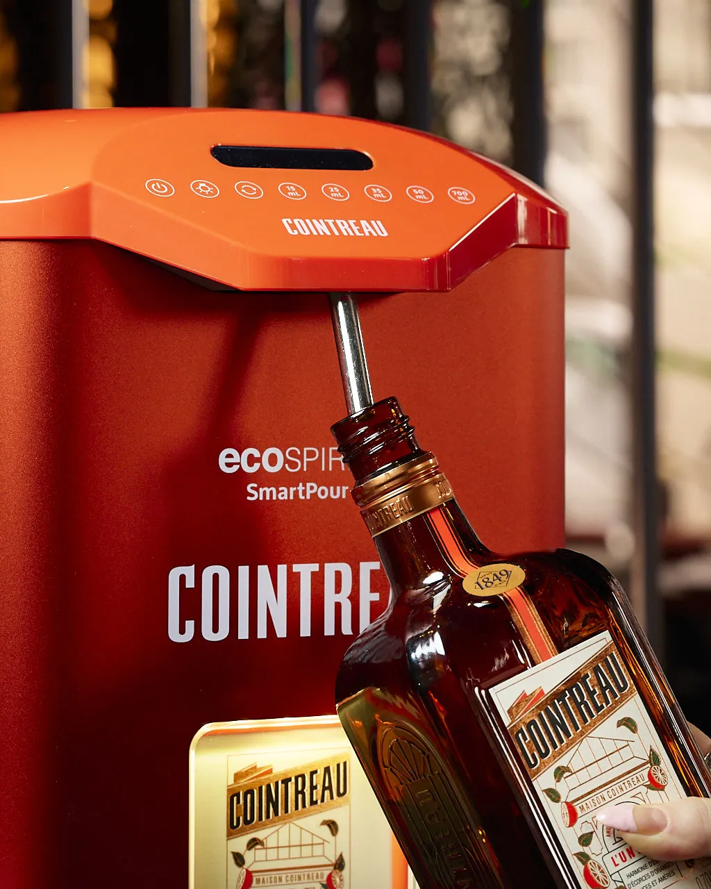 Cointreau bottle held beneath an automated SmartPour dispensing machine branded Cointreau, with the bottle positioned for refilling.