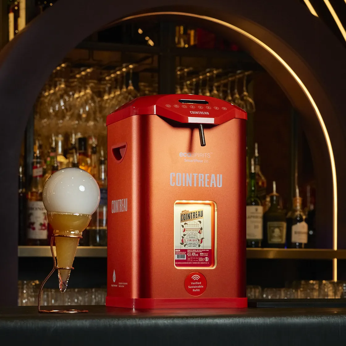 Cointreau SmartPour 2.0 refill station displayed in a bar setting beside a cocktail served in a glass topped with a large bubble garnish.