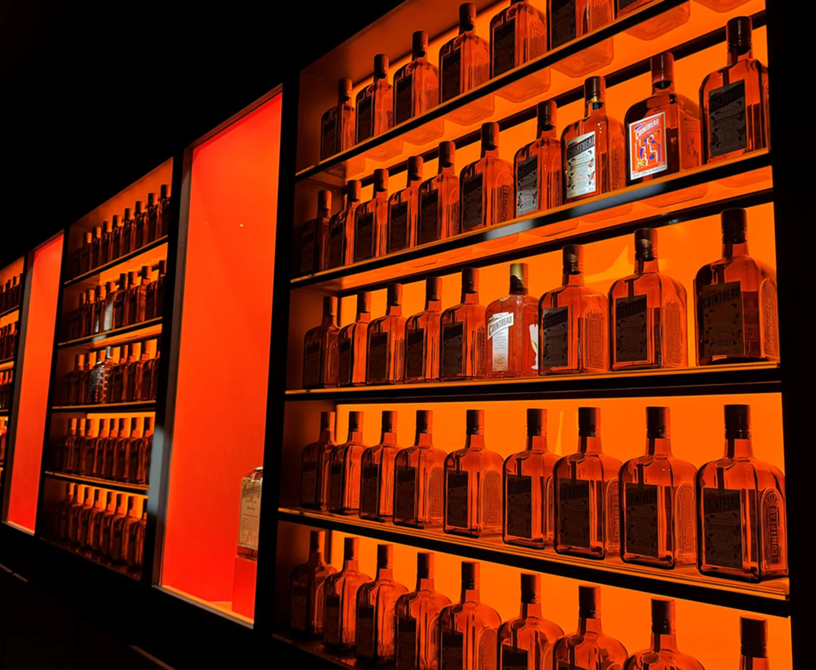Shelves of Cointreau bottles illuminated in warm orange lighting in bar display