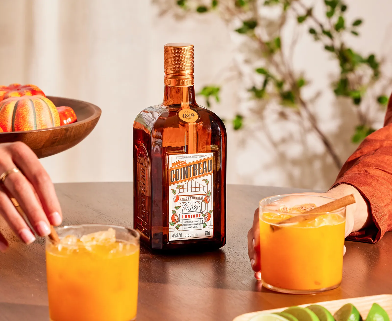 Cointreau bottle with orange cocktails in glasses on table with citrus garnish and spices