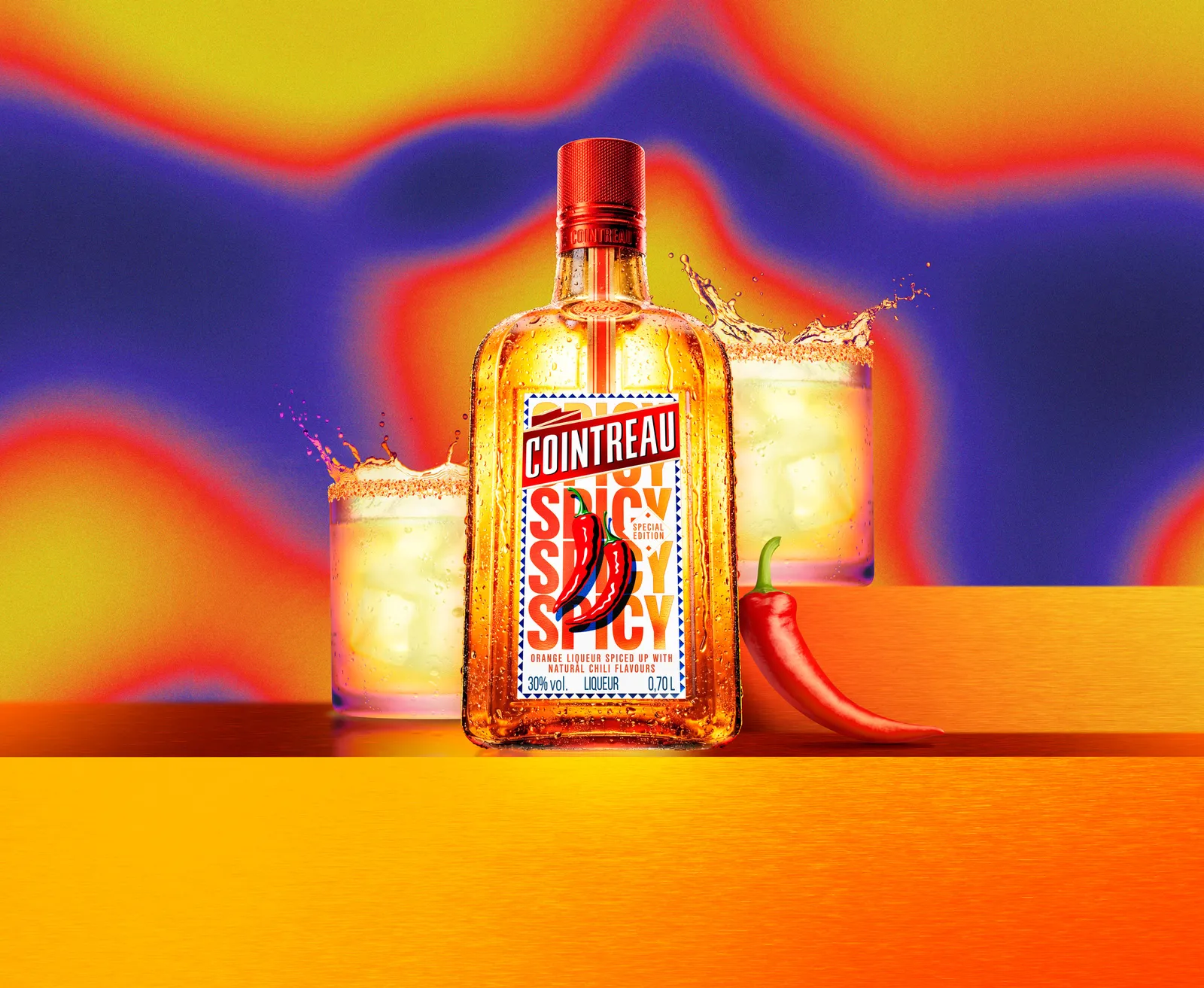 Cointreau Spicy bottle with chilli graphic centred between two tumbler glasses, splashes and red chilli on vibrant gradient background