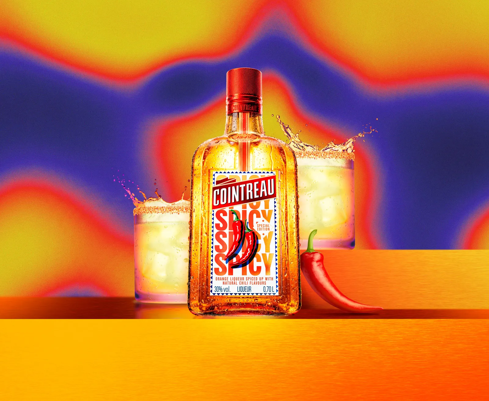Cointreau Spicy bottle with chilli graphic centred between two tumbler glasses, splashes and red chilli on vibrant gradient background