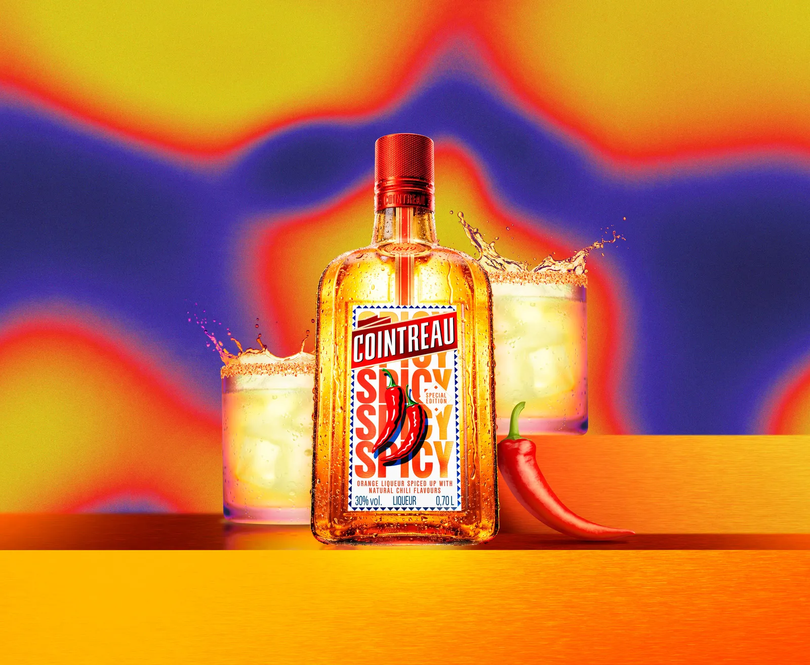 Cointreau Spicy bottle with chilli graphic centred between two tumbler glasses, splashes and red chilli on vibrant gradient background