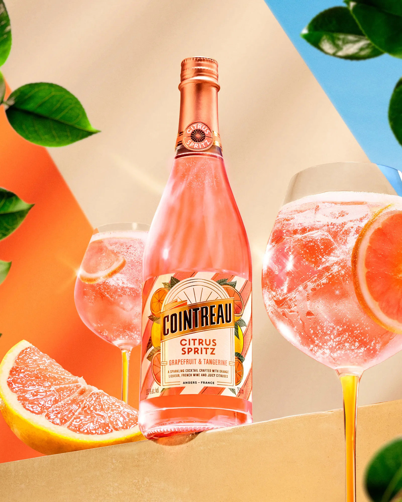 Cointreau Citrus Spritz bottle with grapefruit cocktails, fresh citrus and leaves on bright backdrop