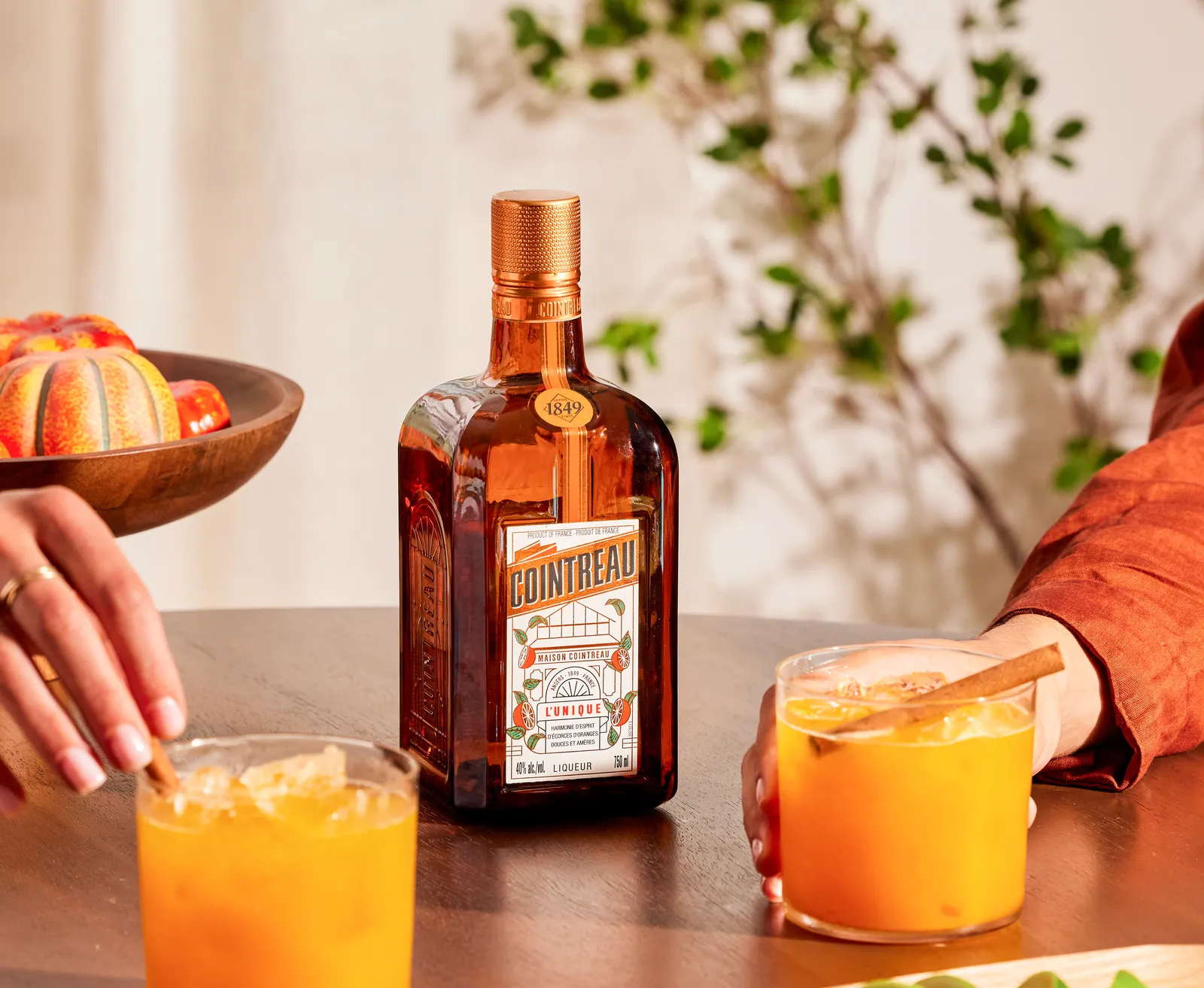 Cointreau orange liqueur bottle with citrus cocktails, lime wedges and fresh ingredients on wooden table