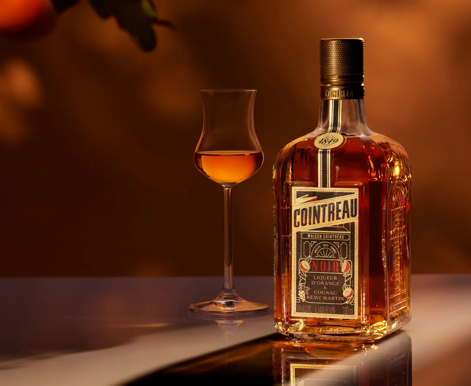 Cointreau Noir orange liqueur bottle with tasting glass on warm amber background