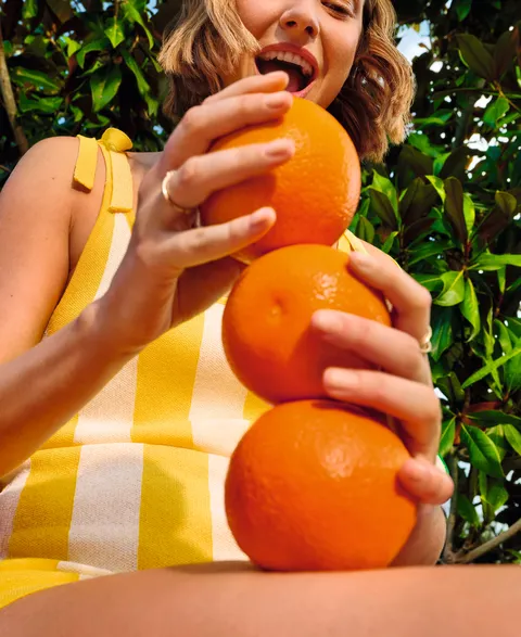 Person holding fresh oranges in garden with green leaves and bright sunlight