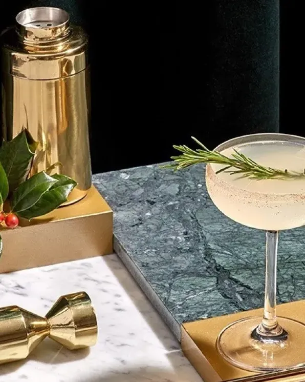 Festive Holiday Margarita served in a coupe glass with a rosemary sprig garnish and cinnamon-sugar rim, surrounded by seasonal holiday accents