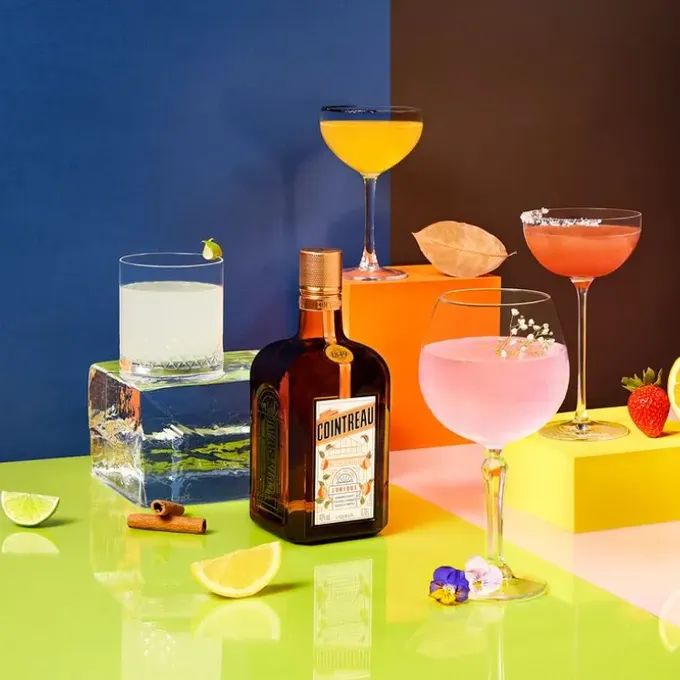 A bottle of Cointreau Orange Liqueur with four different Margaritas on a colorful background