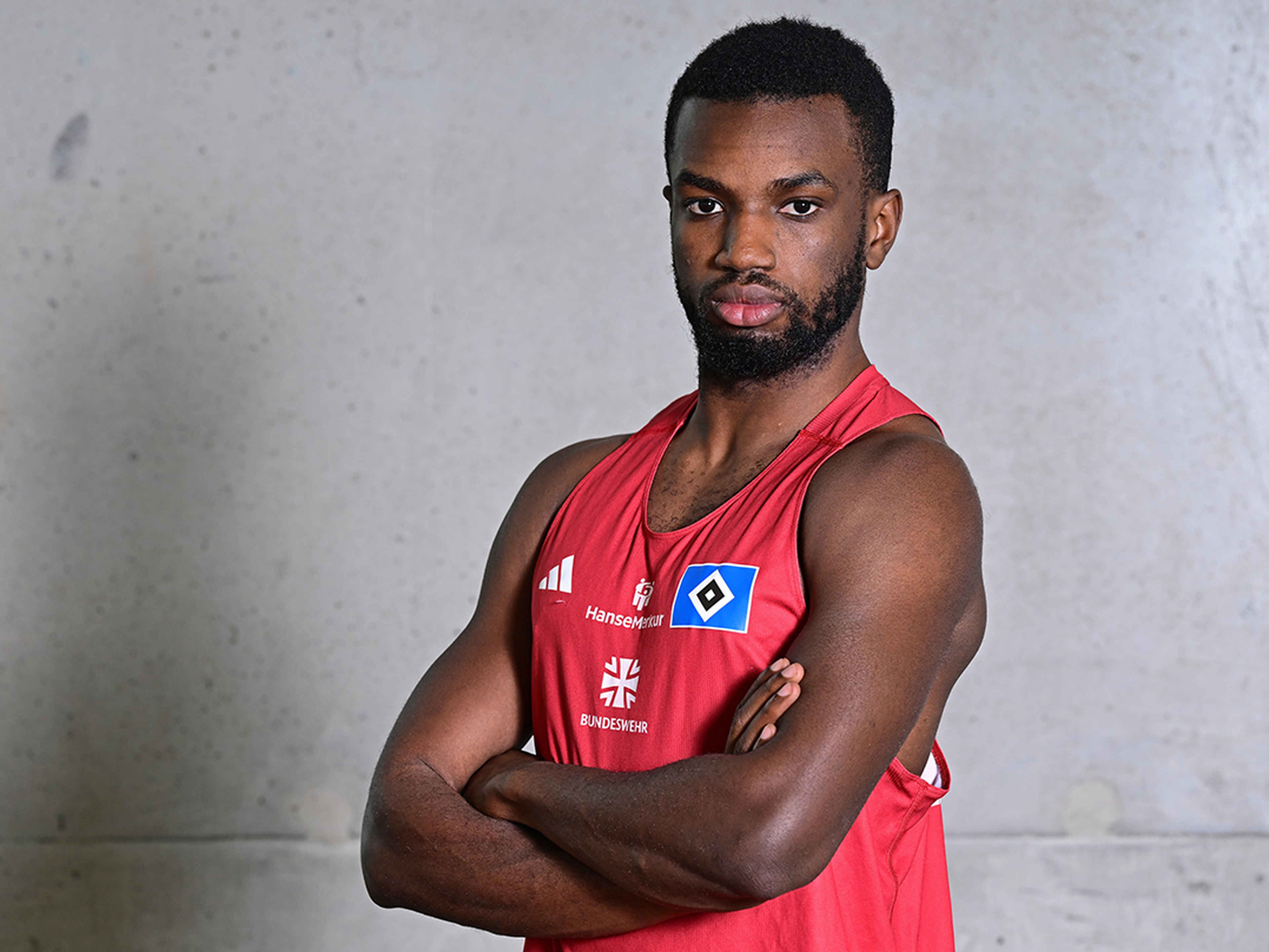 A person in a red sports jersey with crossed arms, standing against a plain background.