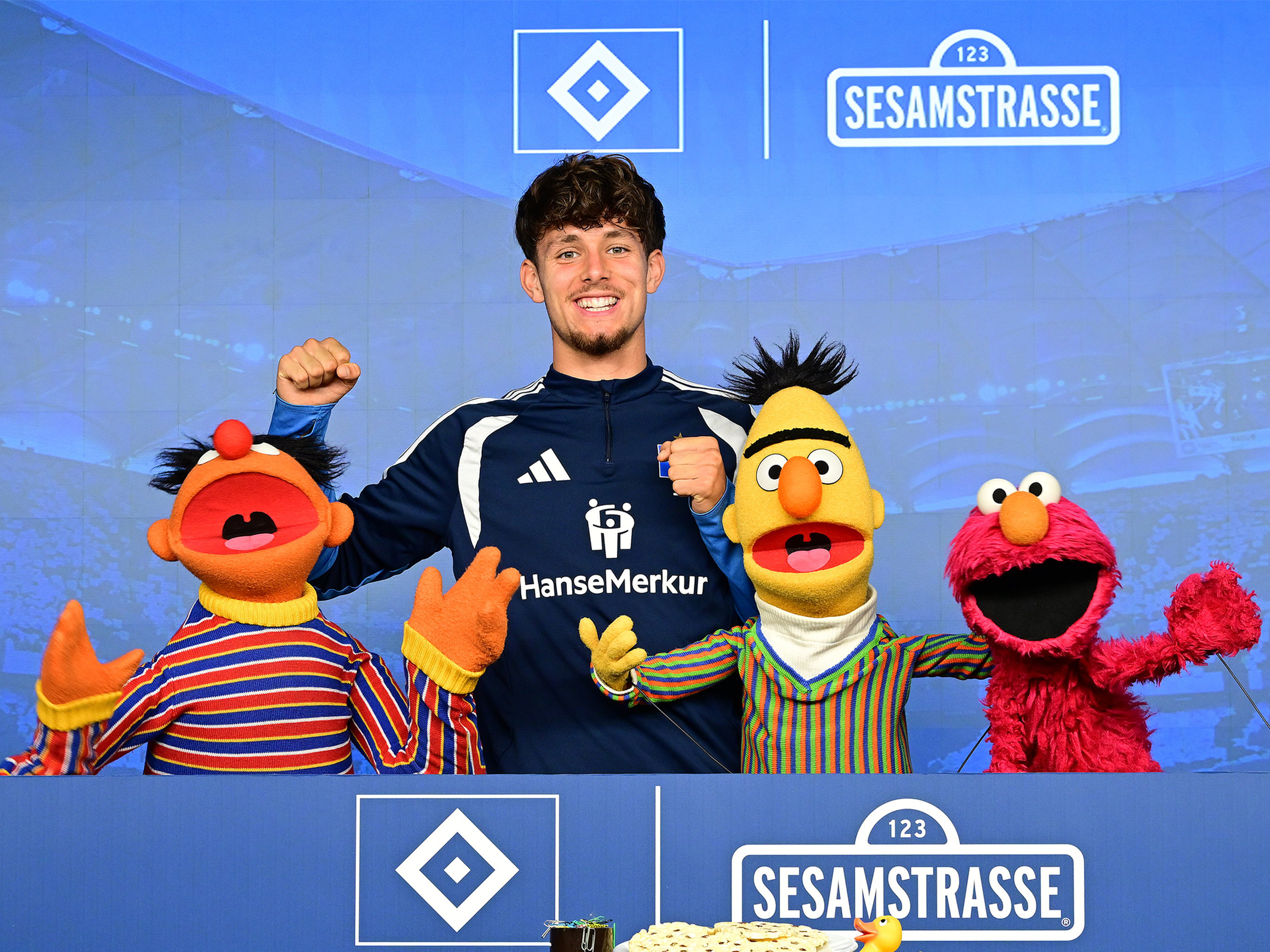 HSV-Spieler Otto Stange posiert mit Charakteren der Sesamstraße.
