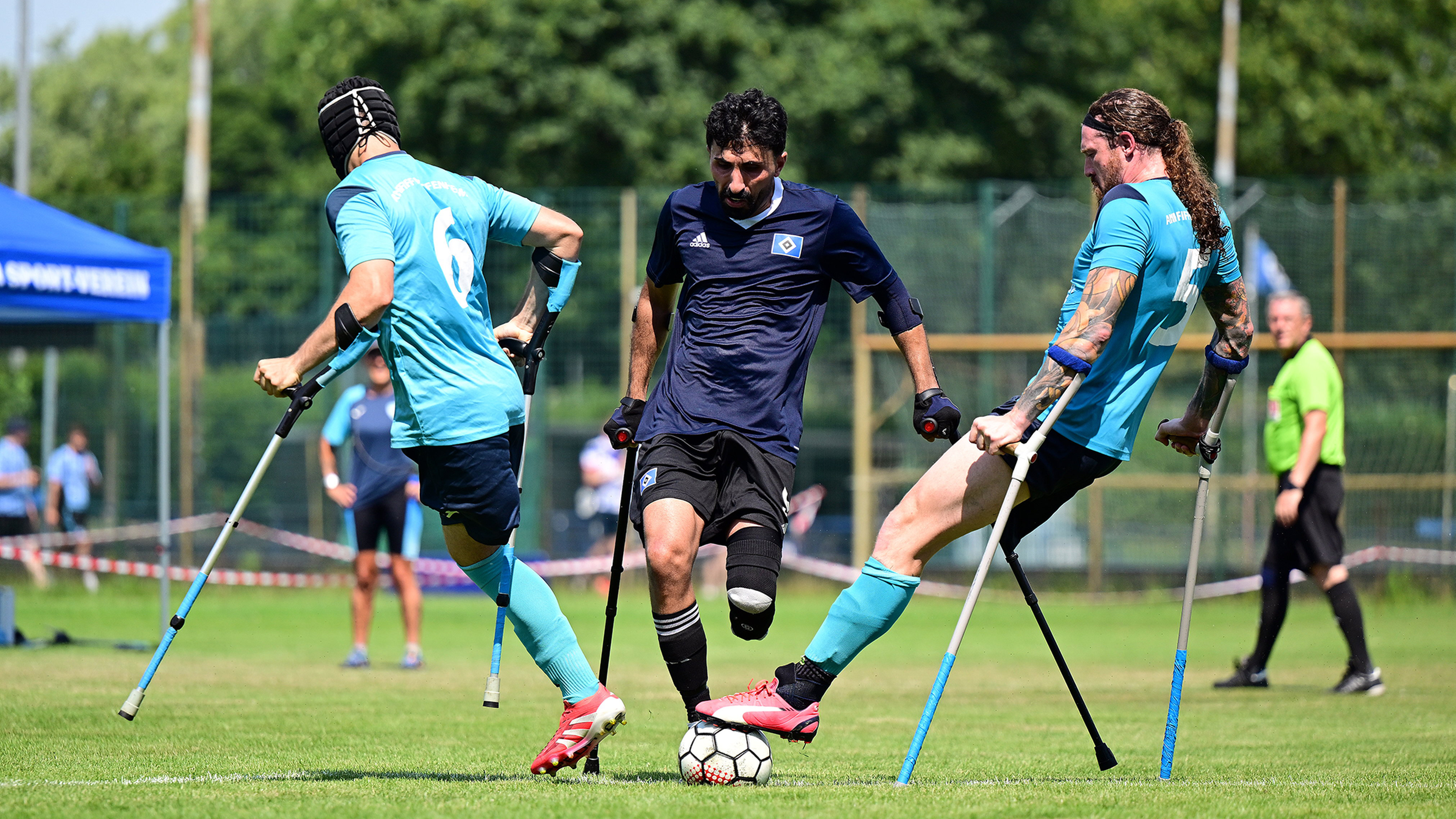 Three athletes playing amputee football fiercely contest the ball on a grassy field, all supported by crutches.