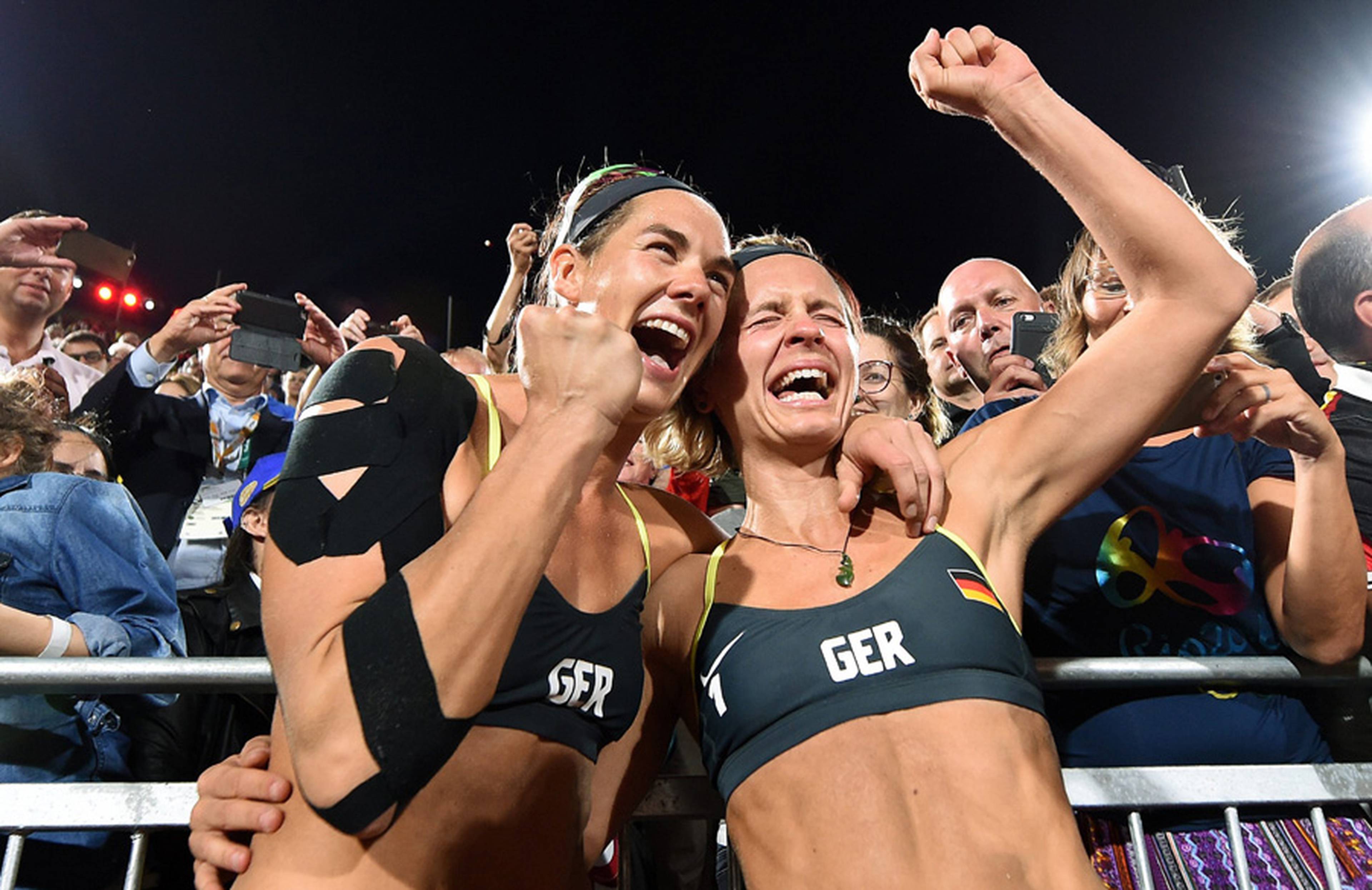 Kira Walkenhorst und Laura Ludwig stehen feiernd vor der Tribüne. 