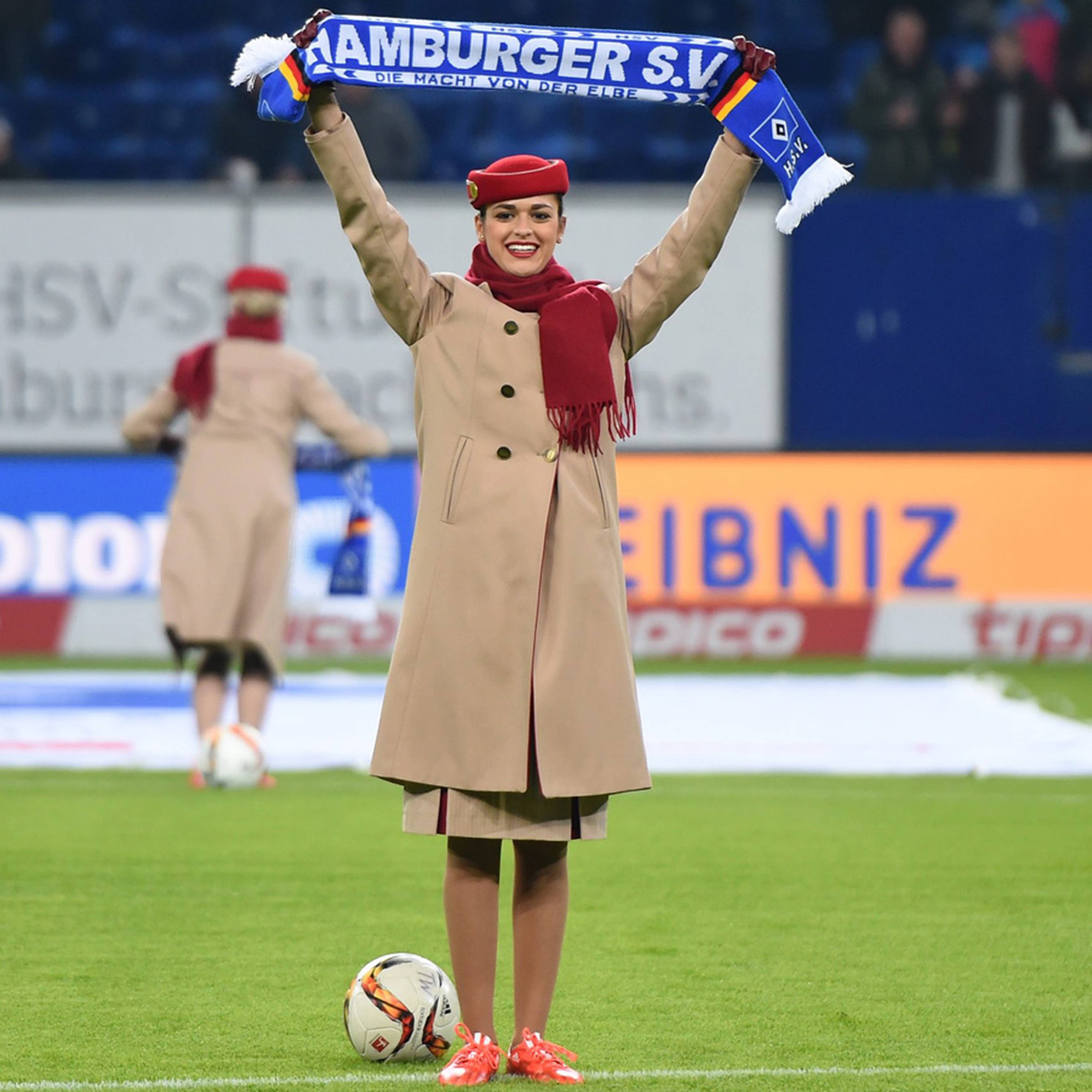 Stewardess gibt mit Schal in beiden Händen eine Anweisung für die Zuschauer. 