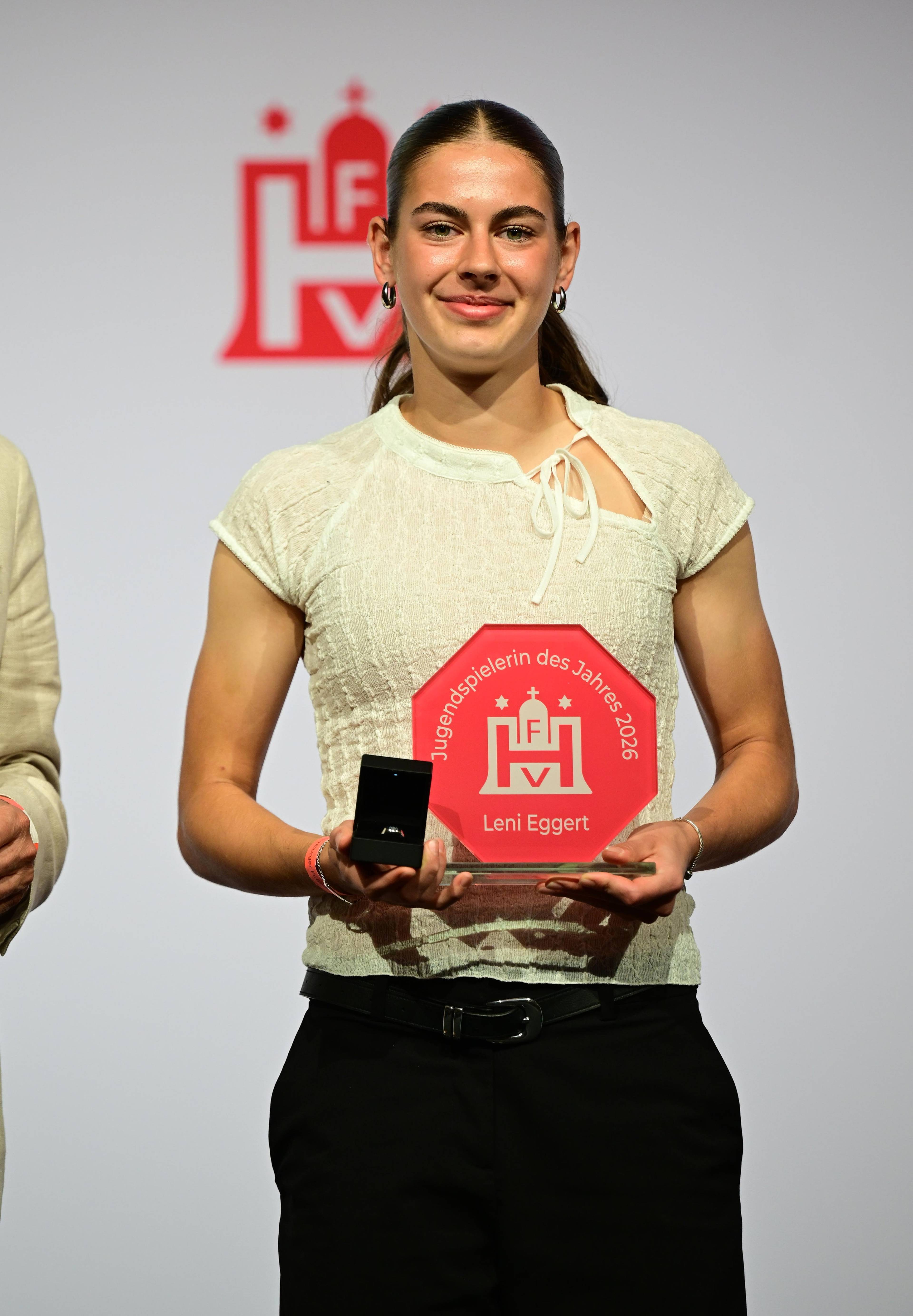A person holding a red award plaque and a small black box on stage, displaying a proud expression.