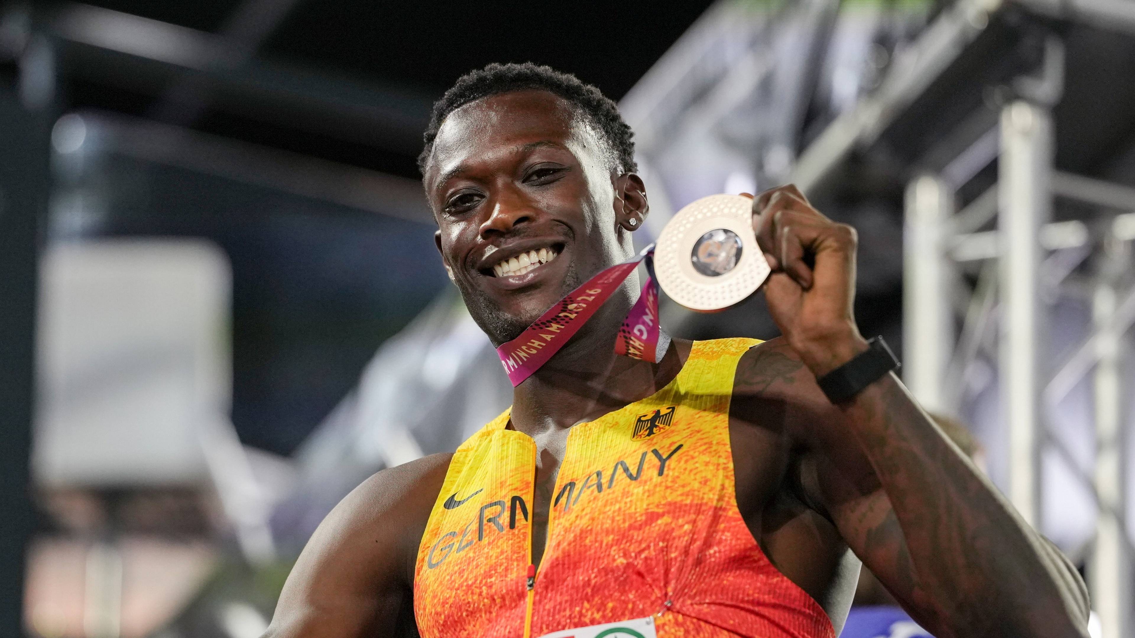 Athlete wearing a German jersey smiles while holding a silver medal, standing on a podium.