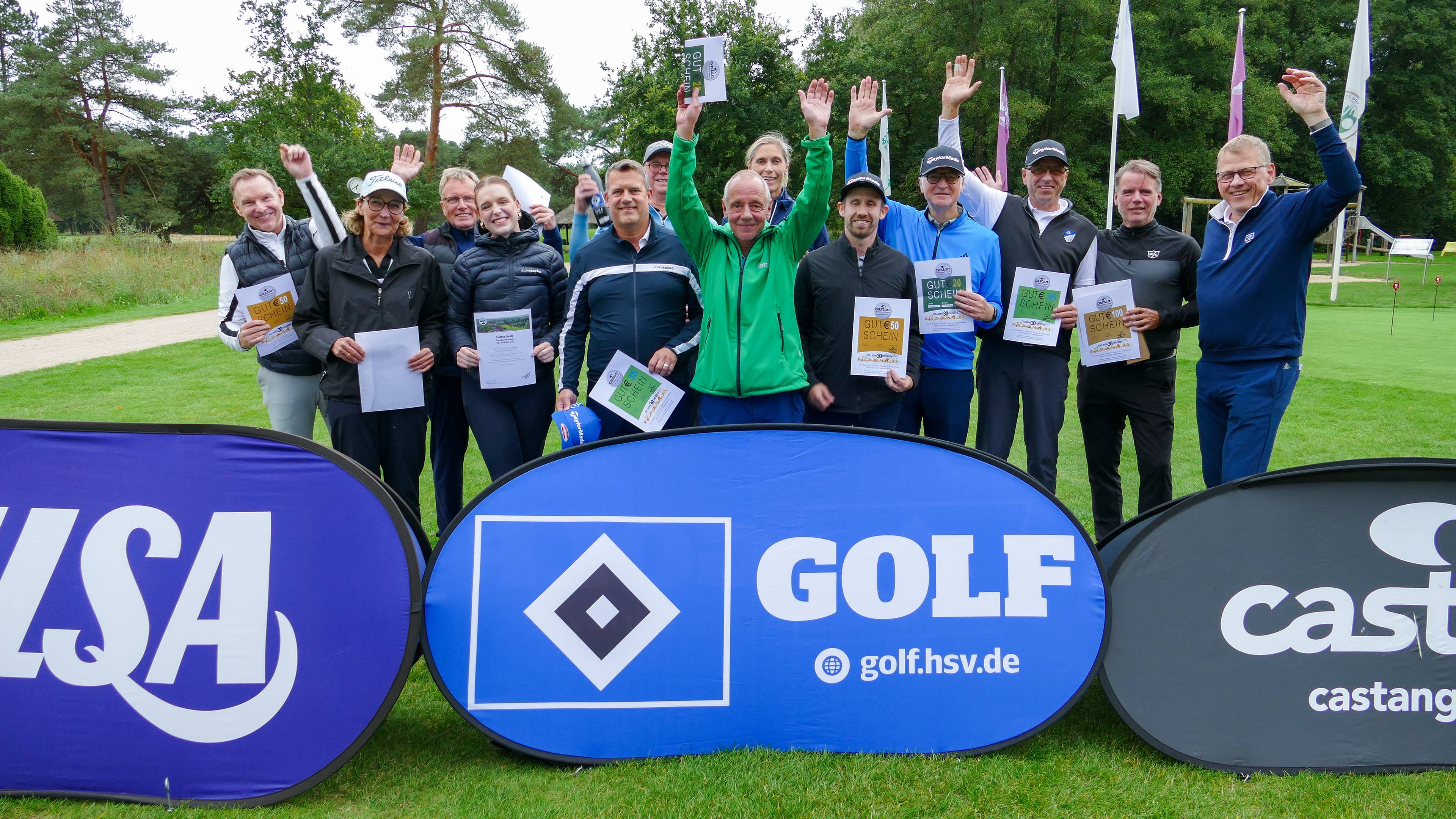 A group of people smiling and holding certificates, standing outdoors on a golf course with banners in the foreground.