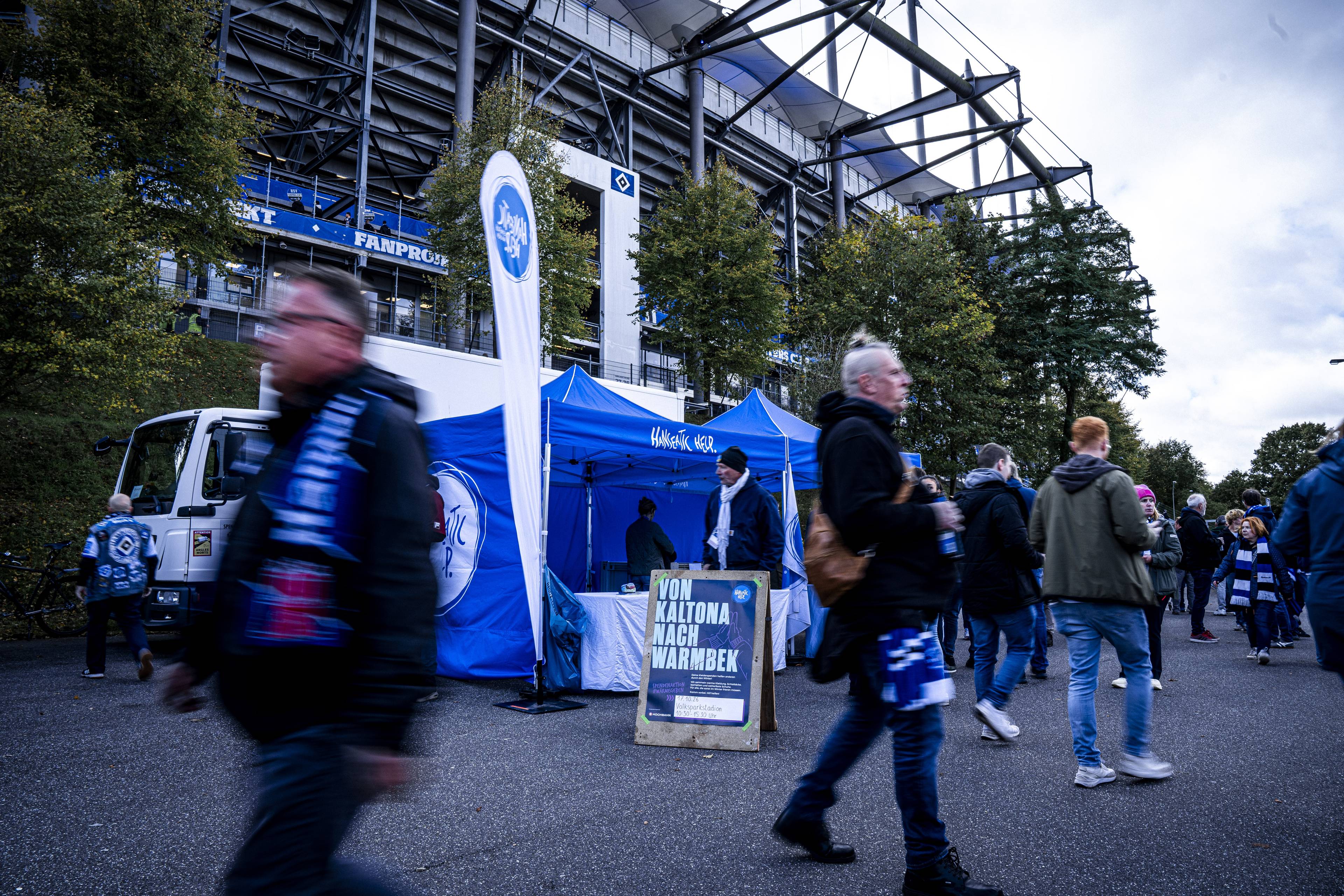 Ein blauer Pavillon von Hanseatic Help vor dem Volksparkstadion. Im Vordergrund laufen HSV-Fans hin und her.
