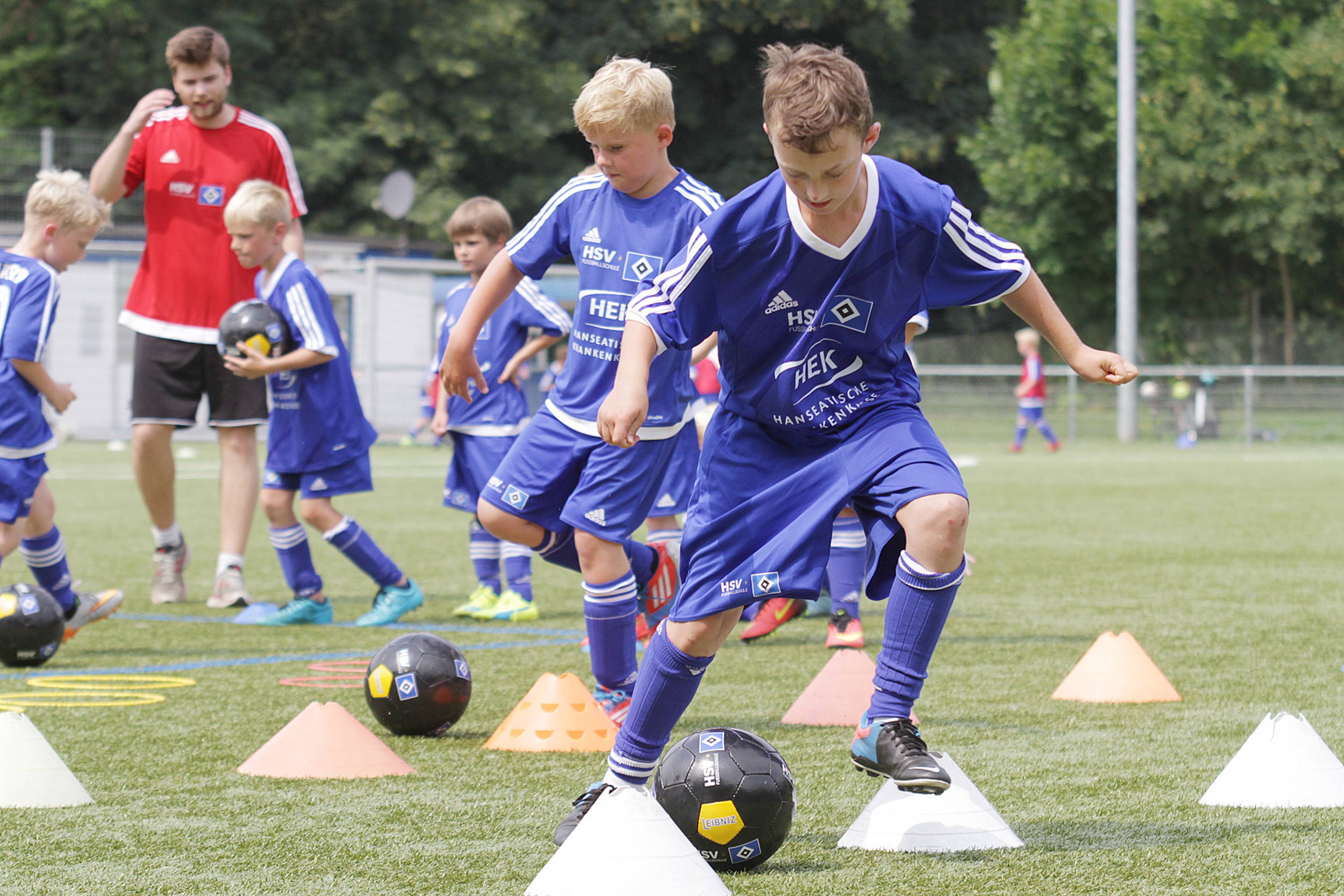 Junge Fußballer spielen den Ball im Slalom um die Pylonen.