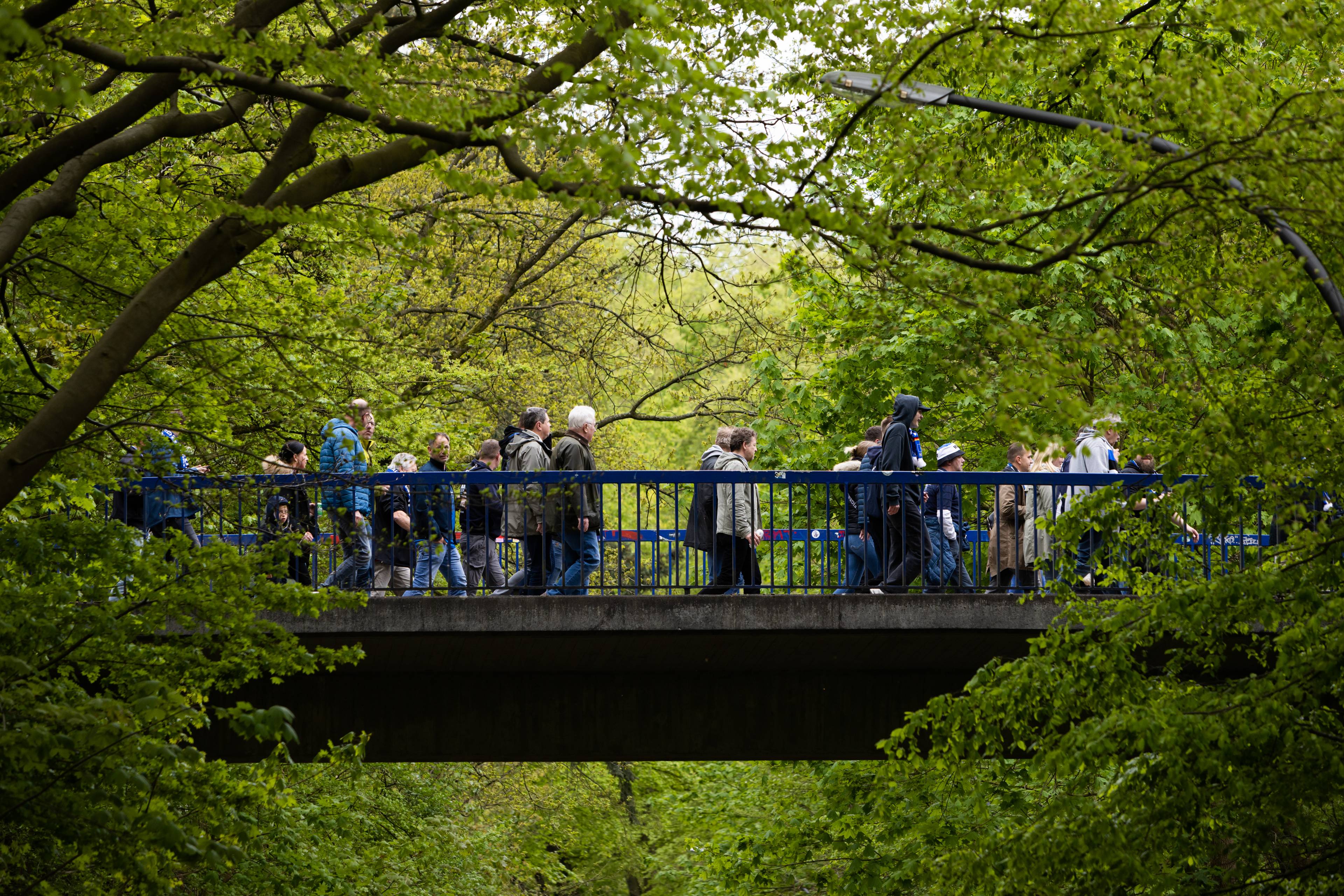 Menschen überqueren eine Brücke in einer grünen Parklandschaft.
