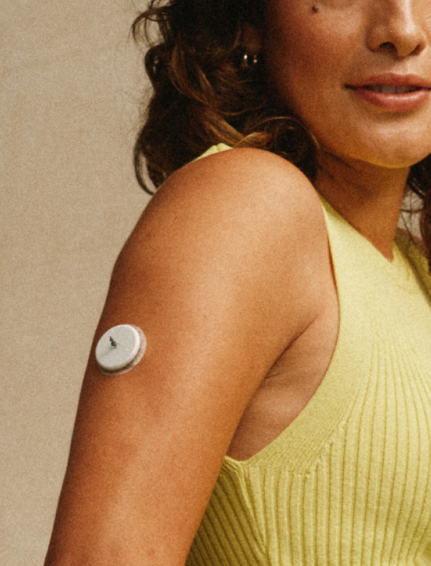 A woman wearing a glucose monitor on her upper arm