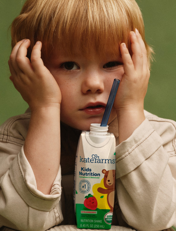A young child holding a carton of Kate Farms Kids Nutrition