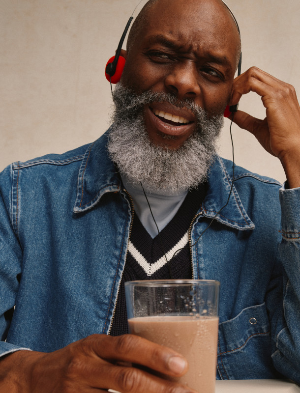 A smiling man with a grey beard and red headphones holding a glass of Kate Farms shake