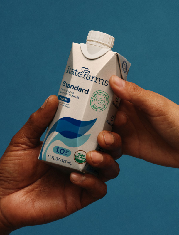 One person handing another a carton of Kate Farms Standard formula
