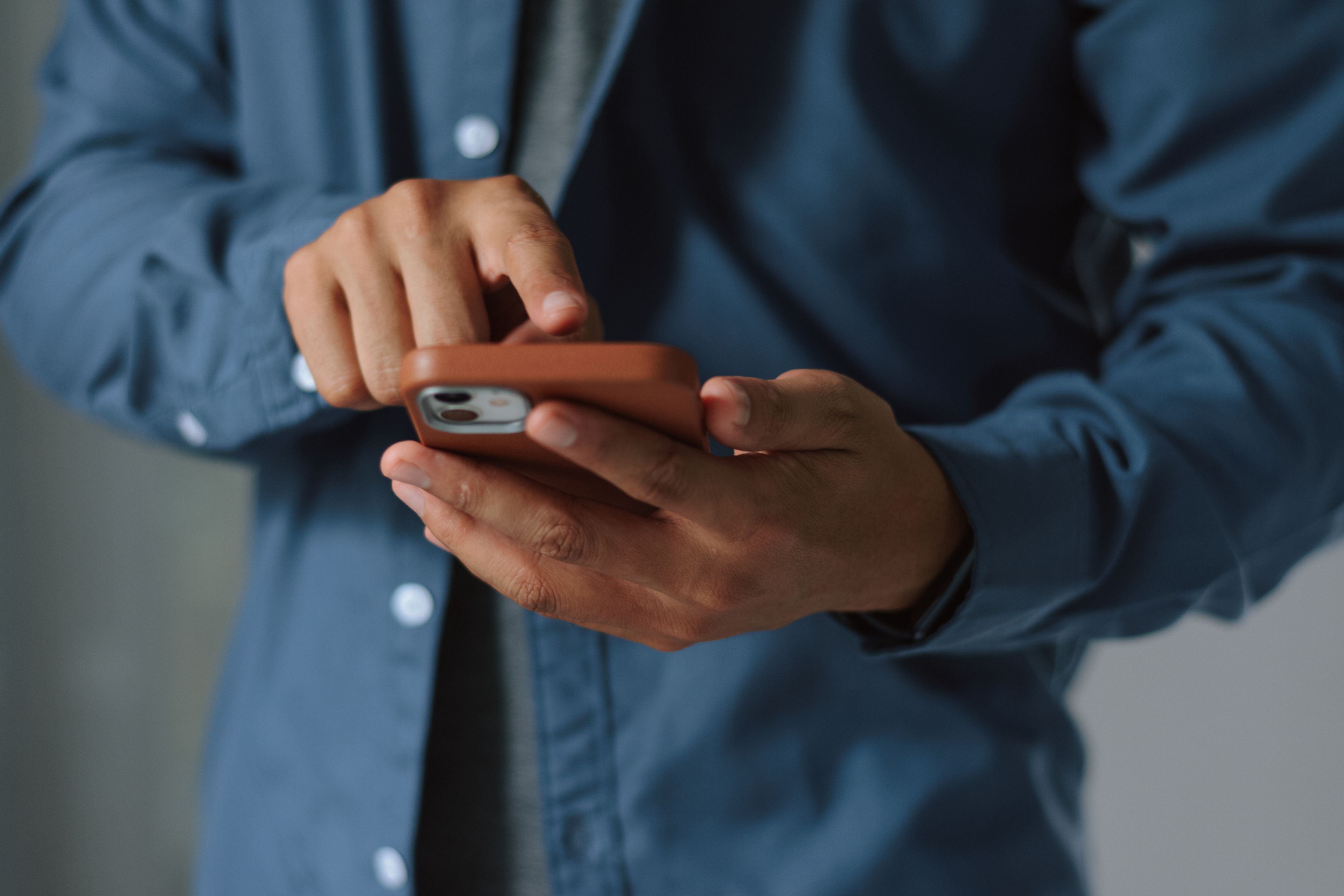 En person i blå skjorta använder en smartphone med ett brunt skal, trycker på skärmen med pekfingret.