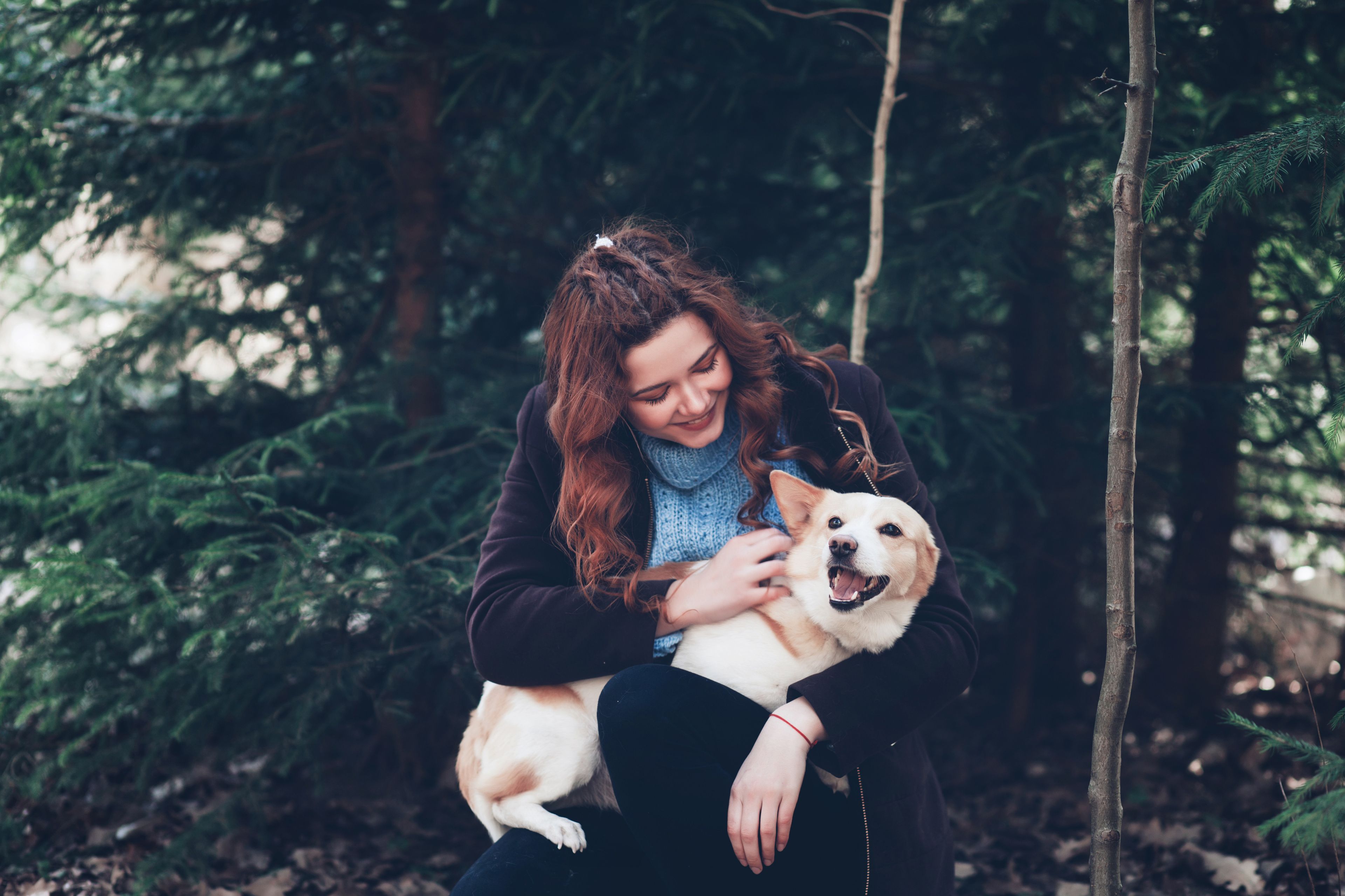 Kvinna kramar en glad hund i skogen, omgiven av gröna träd.