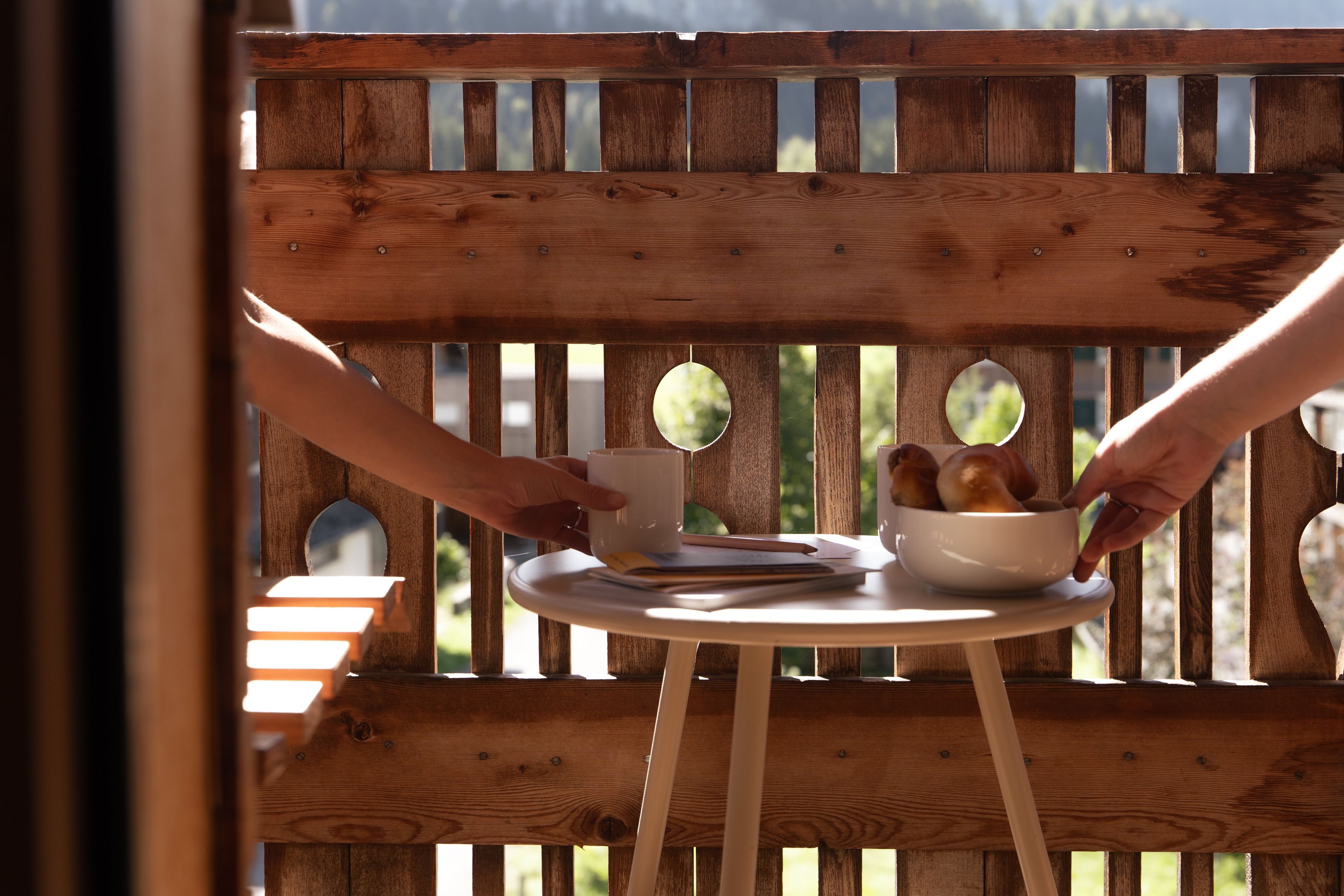 Balkon mit Frühstück und 2 Hände reichen sich den Kaffee und das Brot