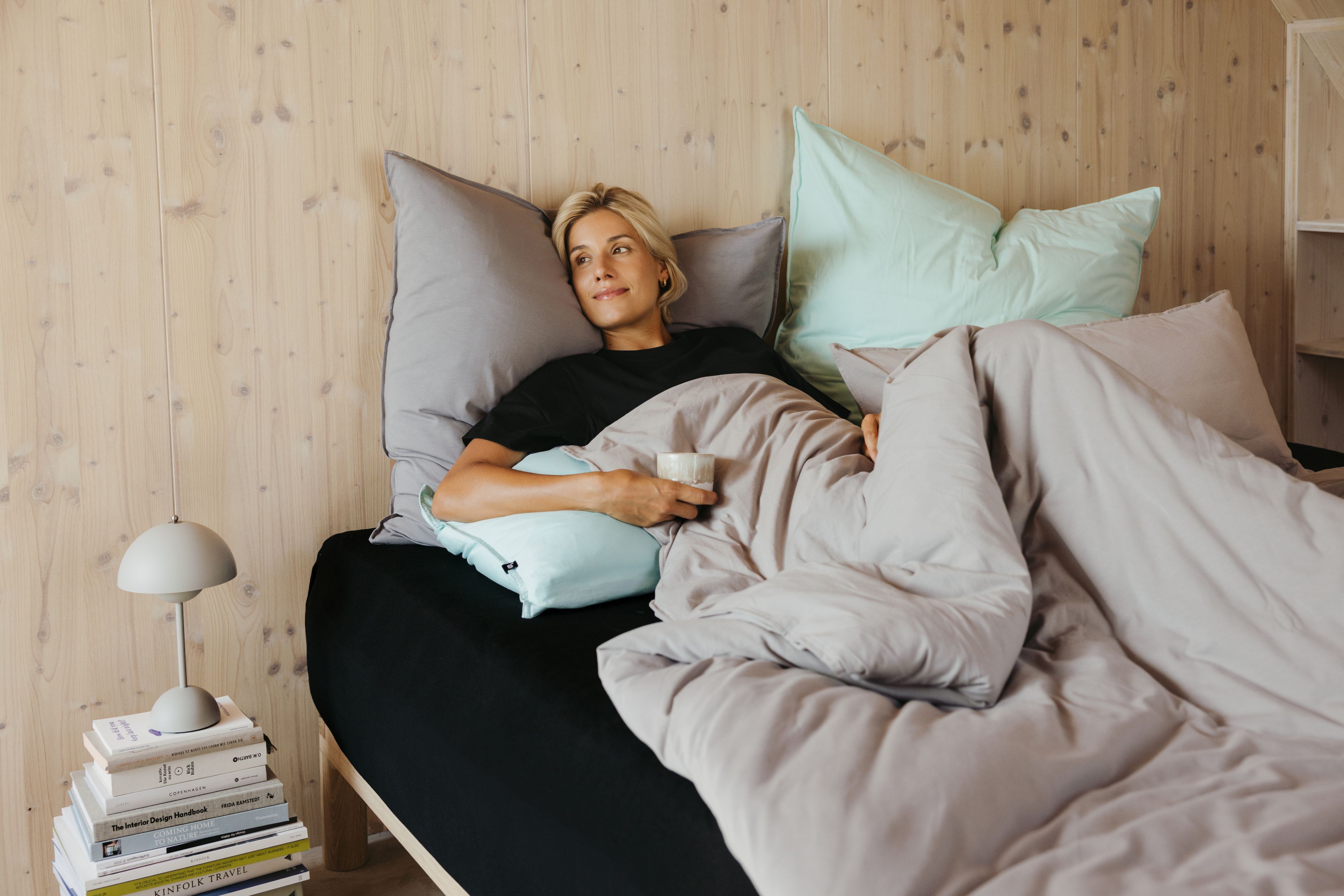Frau liegt im Bett und trinkt Kaffee