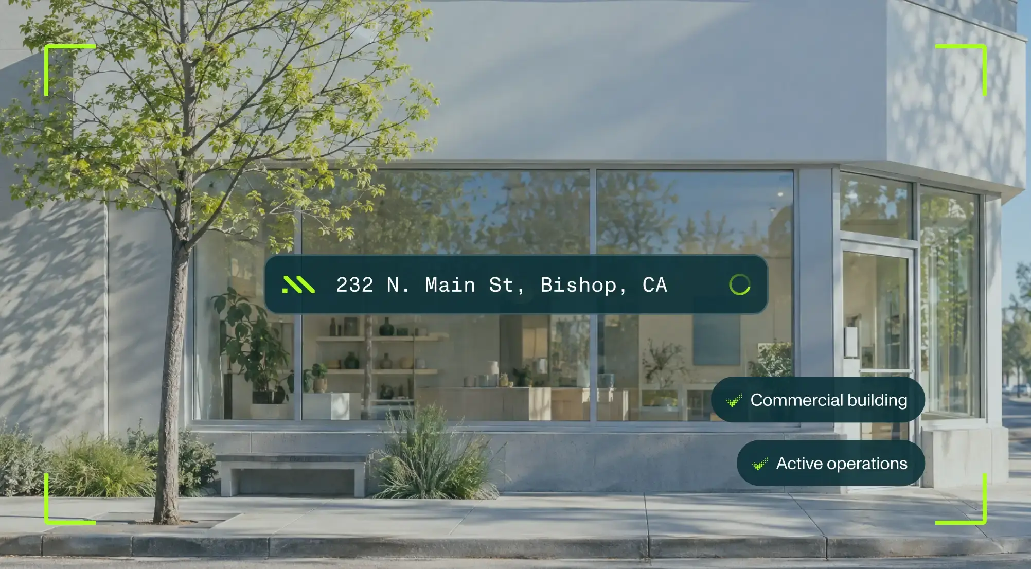 Glass-fronted commercial building with address "232 N. Main St, Bishop, CA" and labels indicating active operations. Tree and plants in foreground.