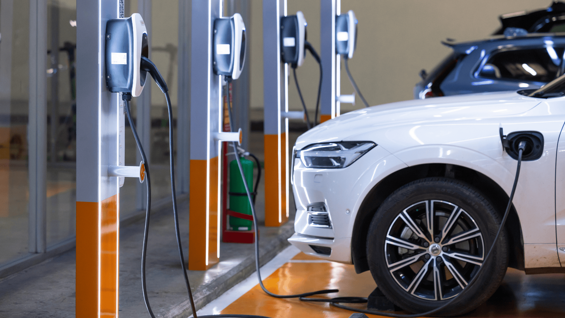Company EV plugged in at a driver's home in the evening, with a fleet depot and a public fast-charging station in the background