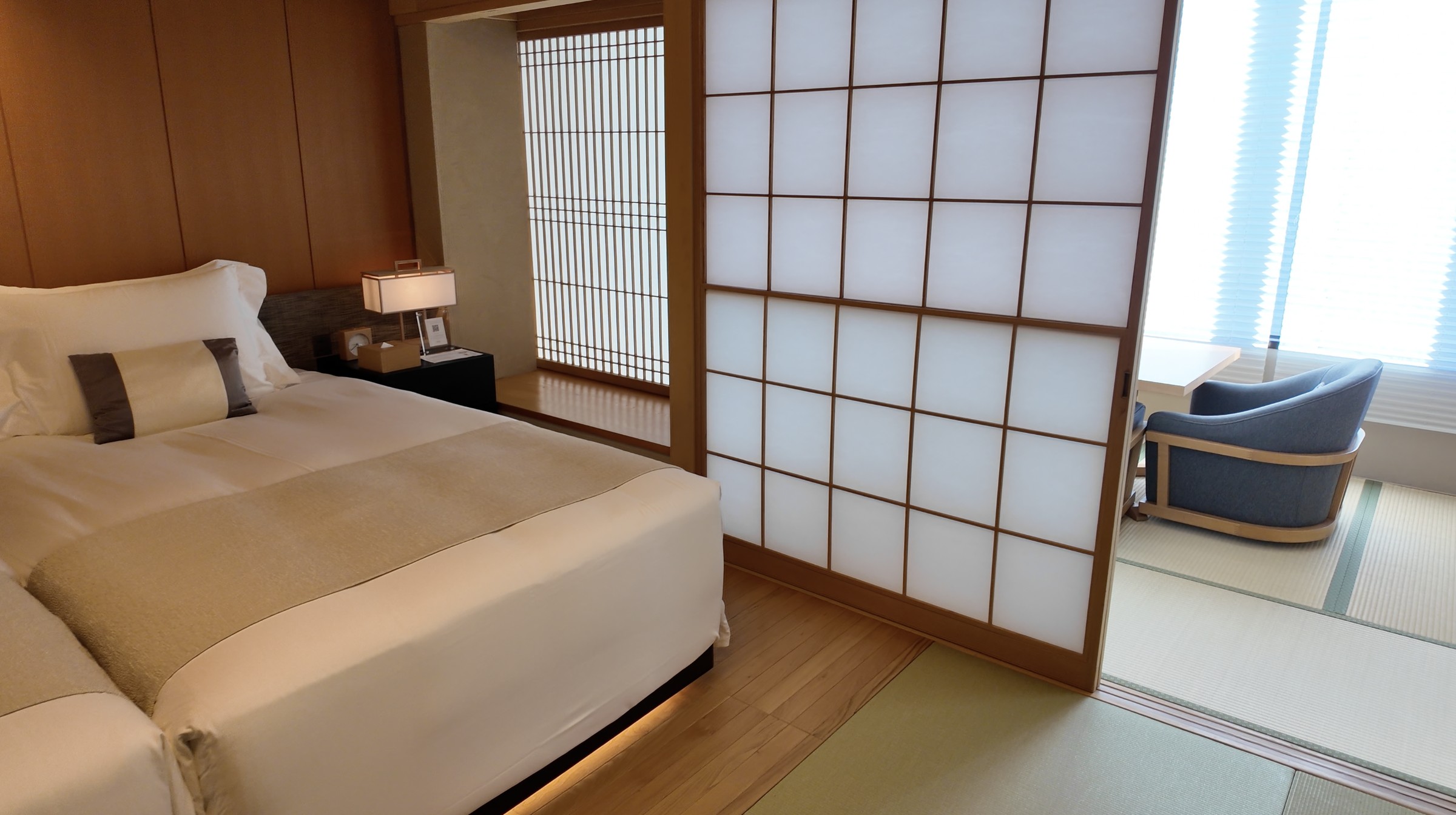 Takanawa Hanakohro suite with a low bed, shoji screens, tatami flooring, and a window-side chair.
