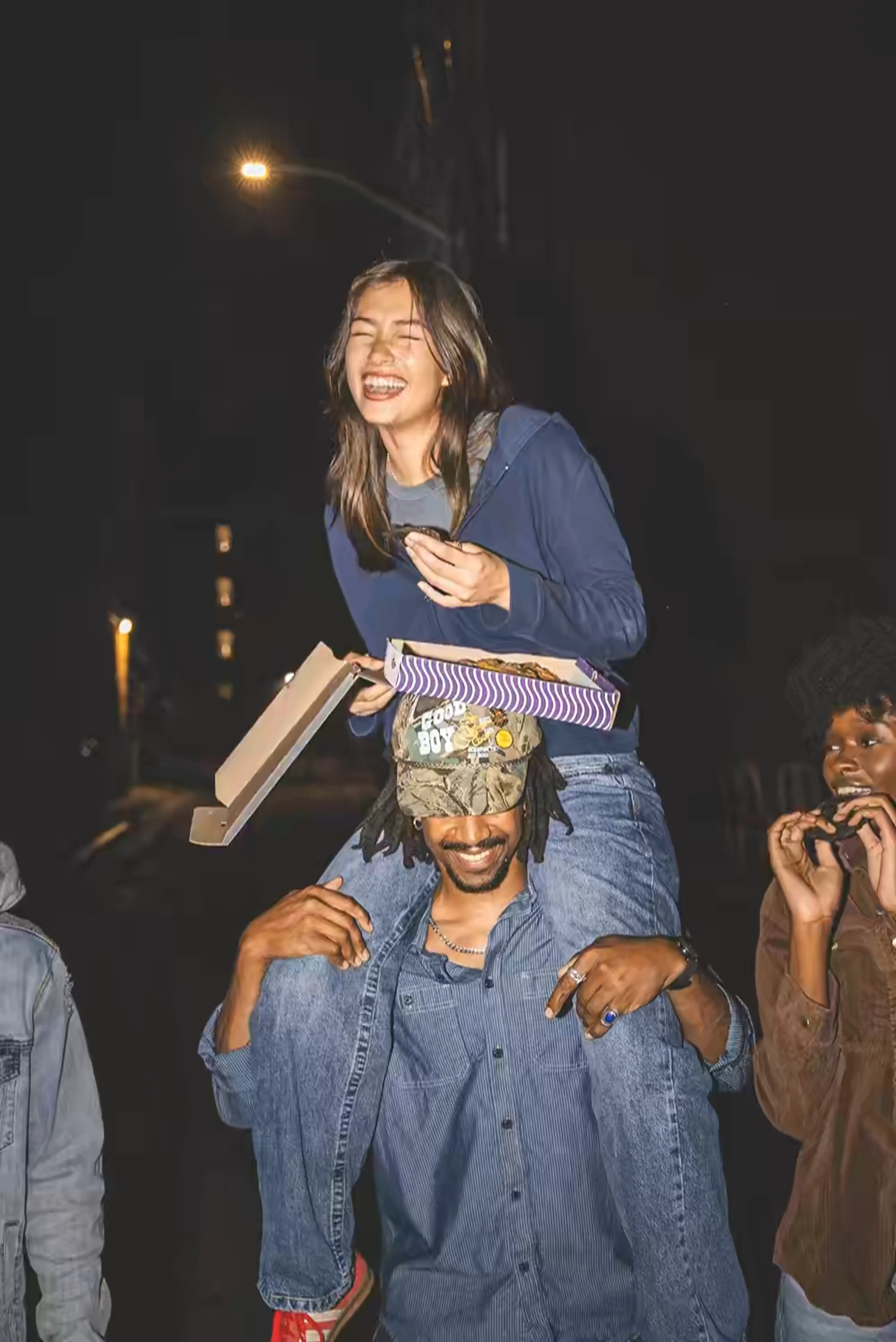 Girl on dudes shoulders with a box of Insomnia Cookies